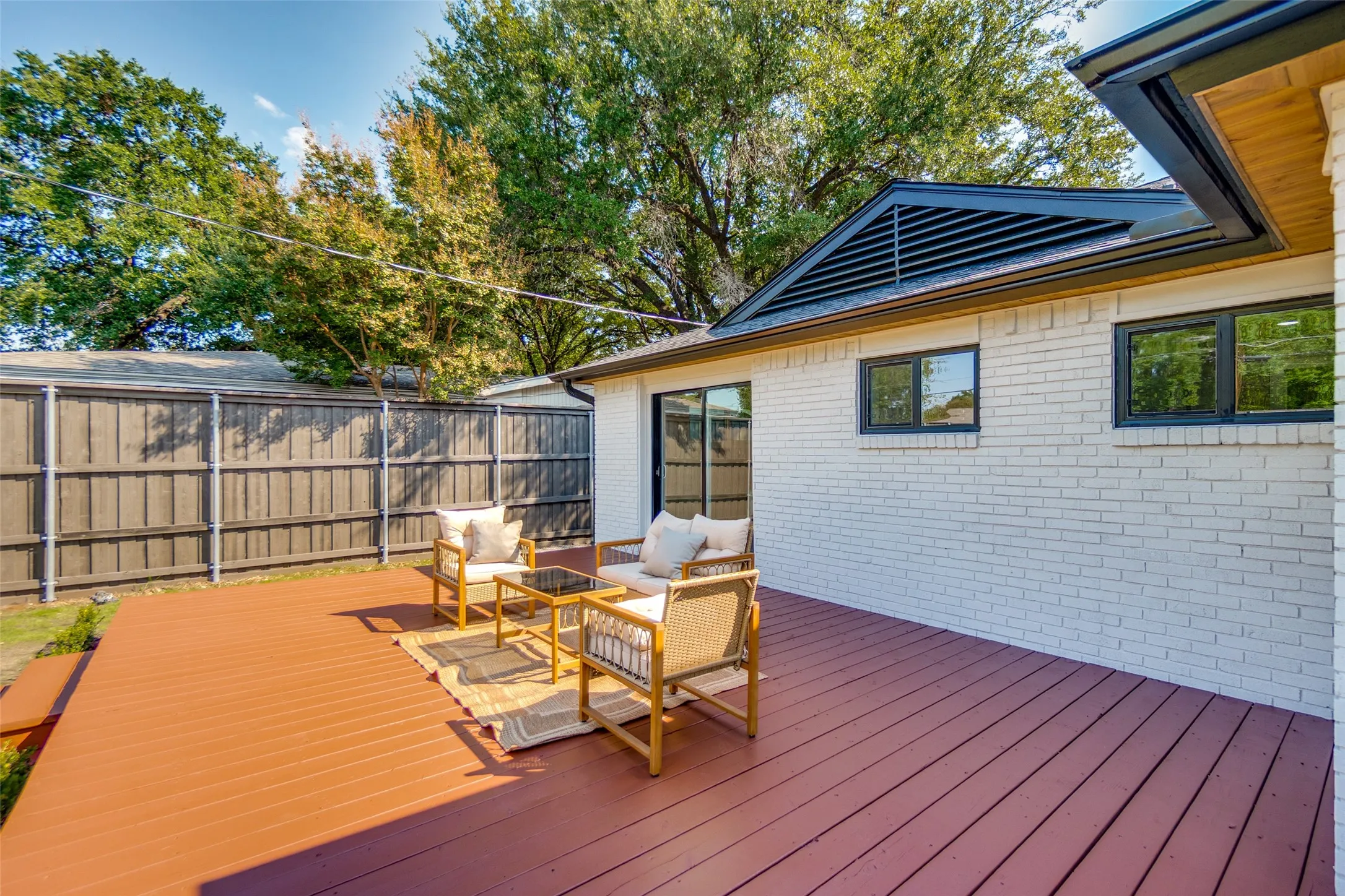 Expansive rear deck, white brick exterior, black frame windows, and dark louvered gable vent