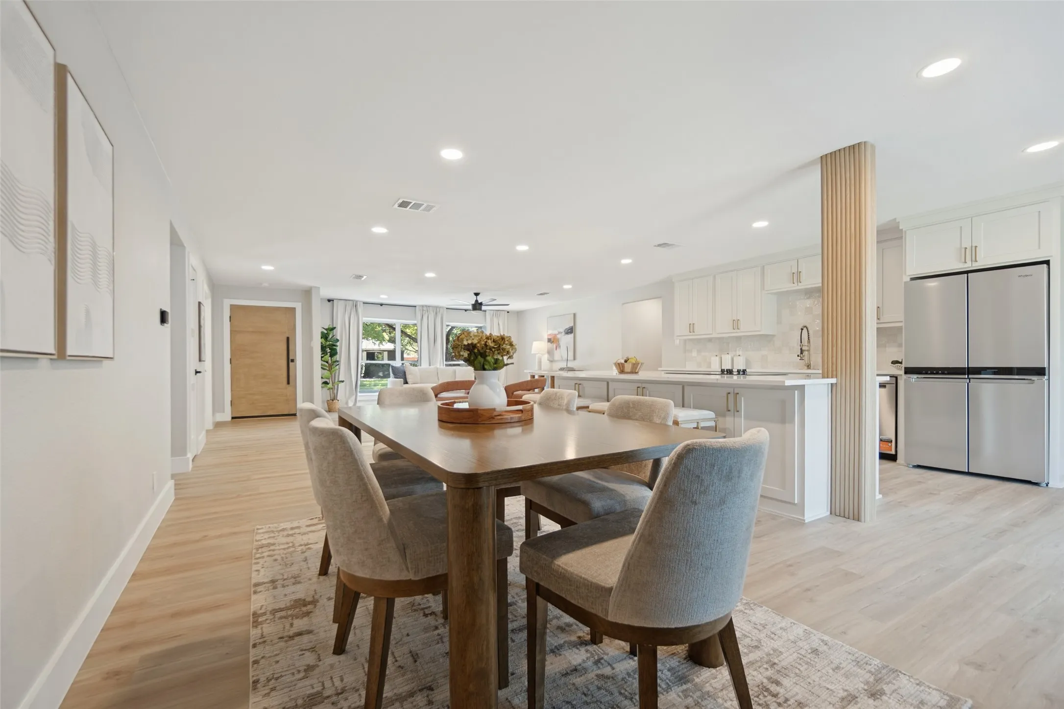Open-concept living space with light wood-finish flooring, recessed lighting, white shaker cabinets, and stainless steel appliances