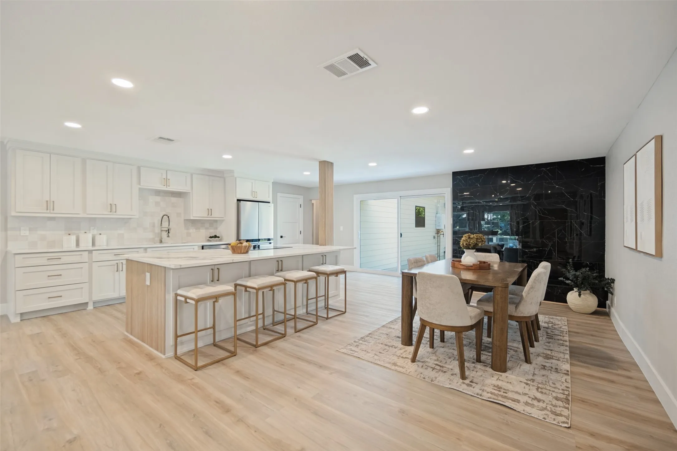 Open-concept living space featuring a kitchen with white cabinetry, a large island with seating, a patterned tile backsplash, and wood-finish flooring