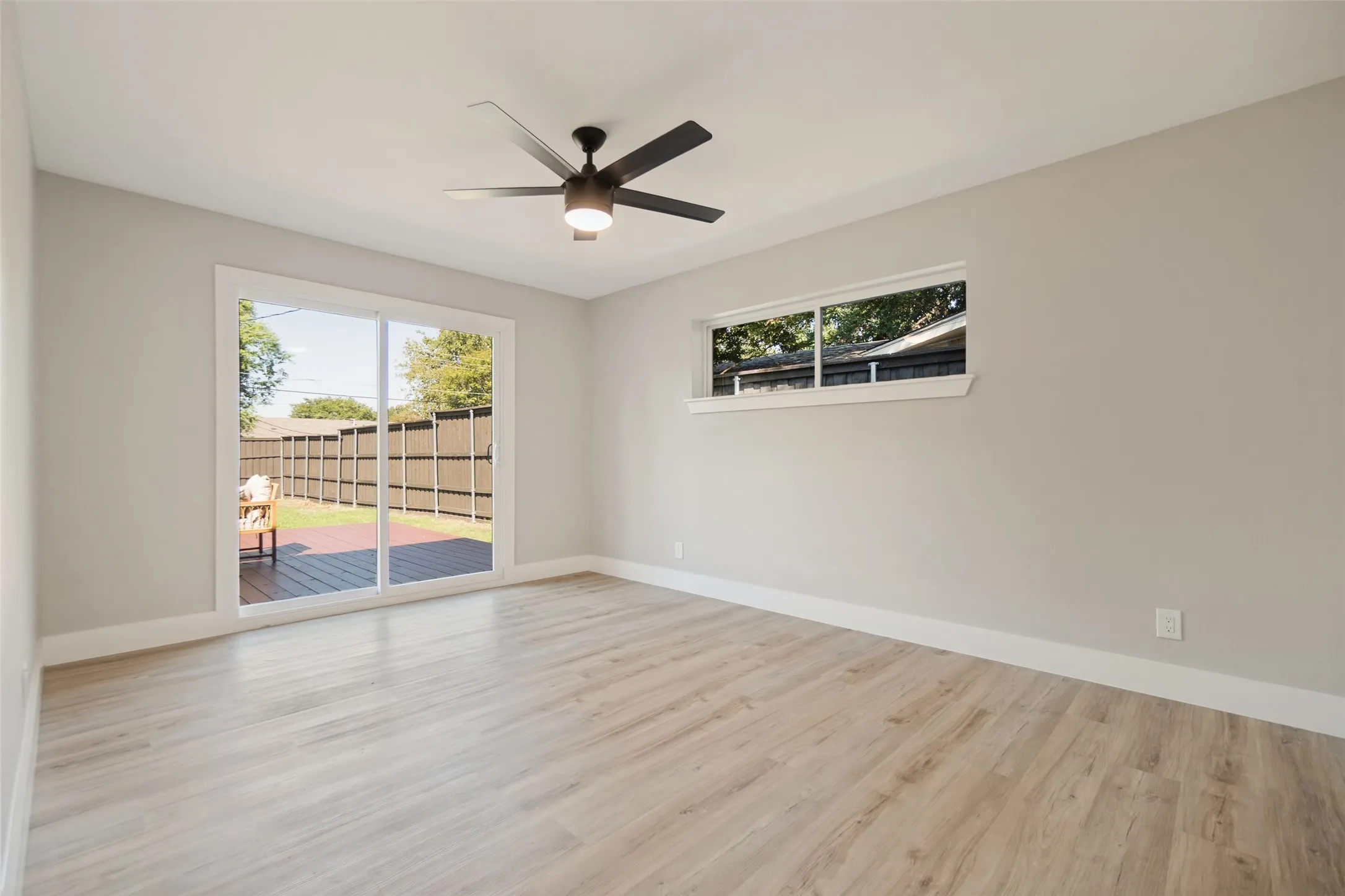 Wood-finish flooring, sliding glass doors to exterior decking, window, ceiling fan with integrated lighting, and neutral wall tones