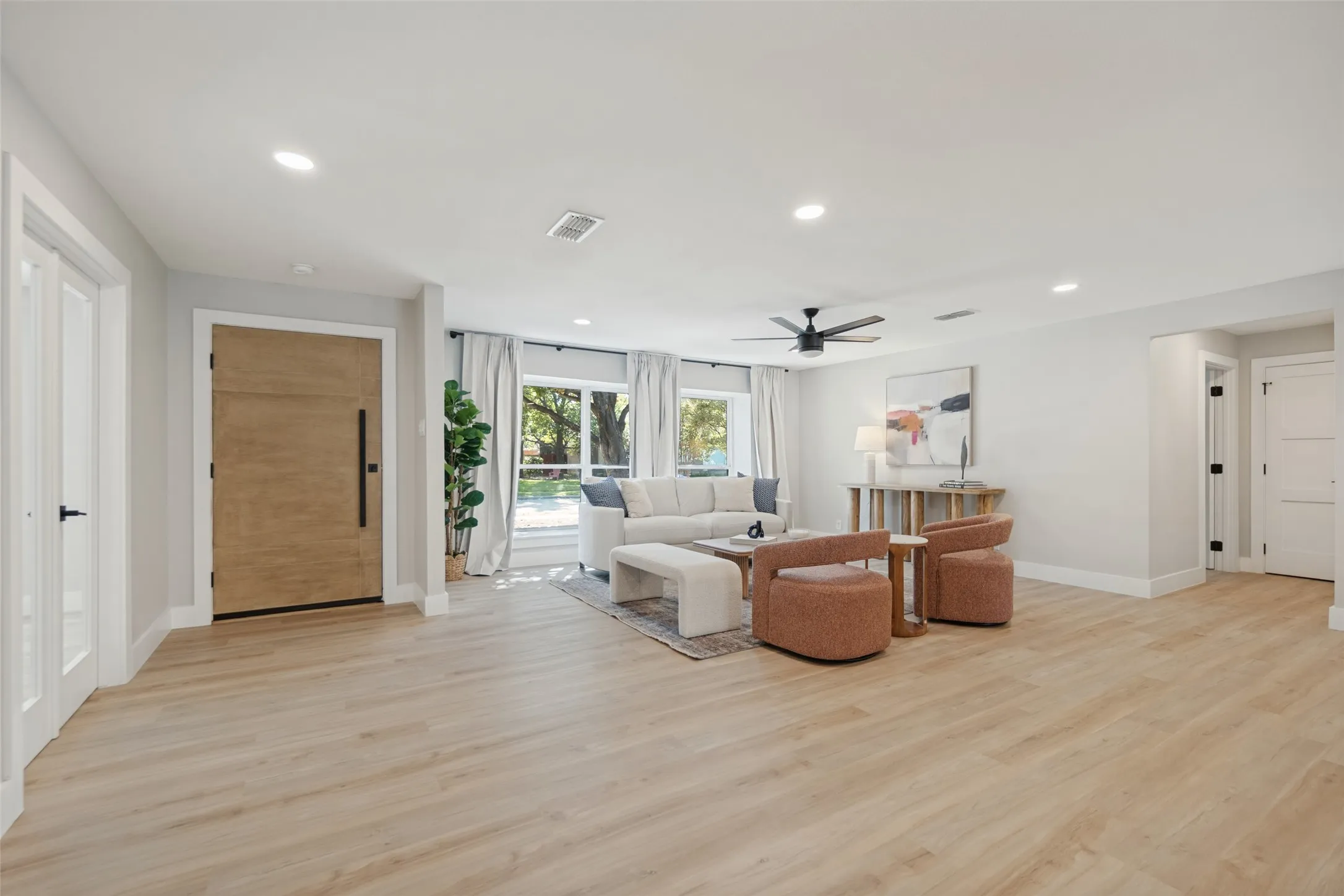 Open-concept living area featuring wood-finish flooring, recessed lighting, a modern ceiling fan, and large windows with white curtains