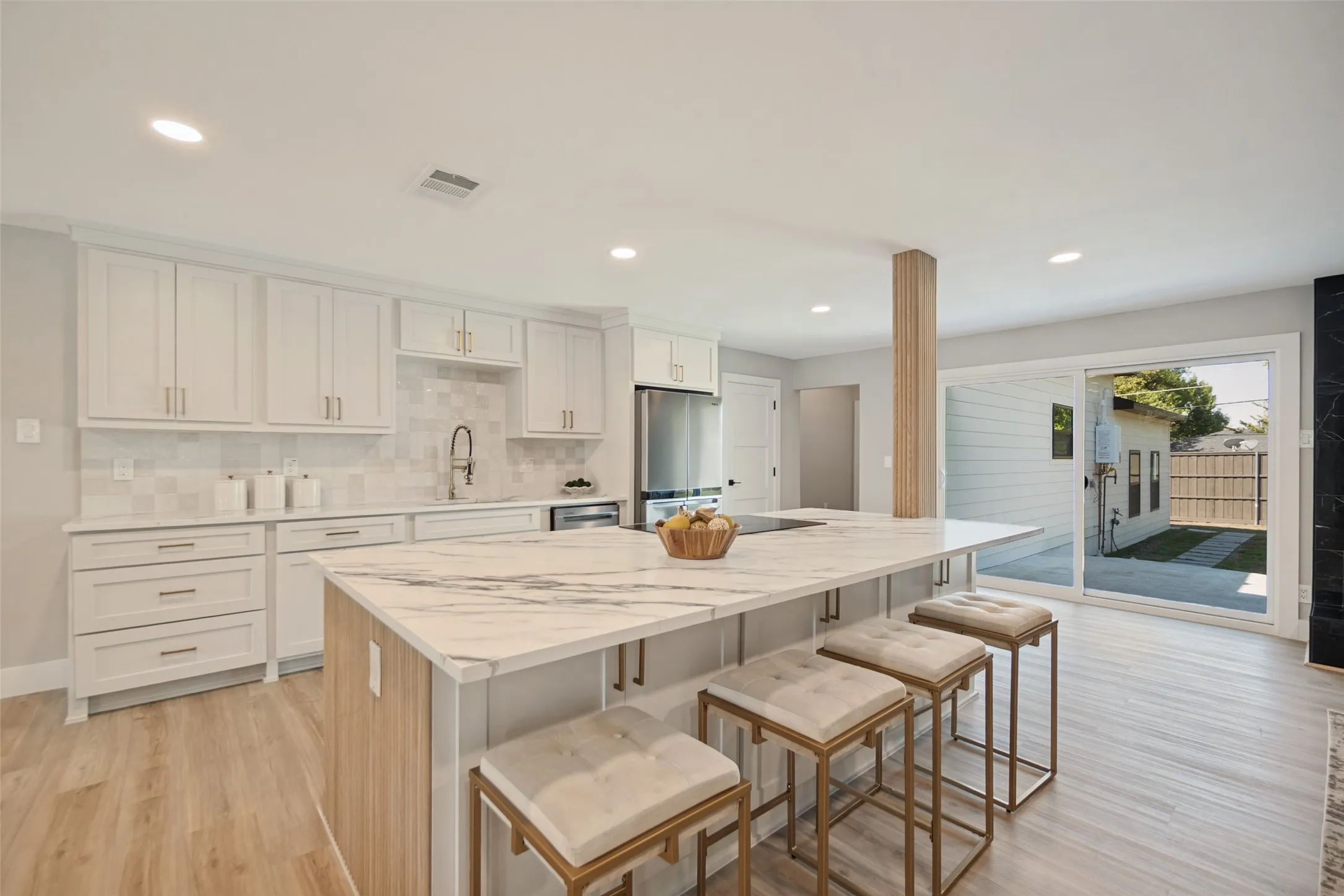 White shaker cabinetry with gold-tone hardware, a large kitchen island with a waterfall countertop, integrated stainless steel appliances, wood-finish flooring, and recessed lighting