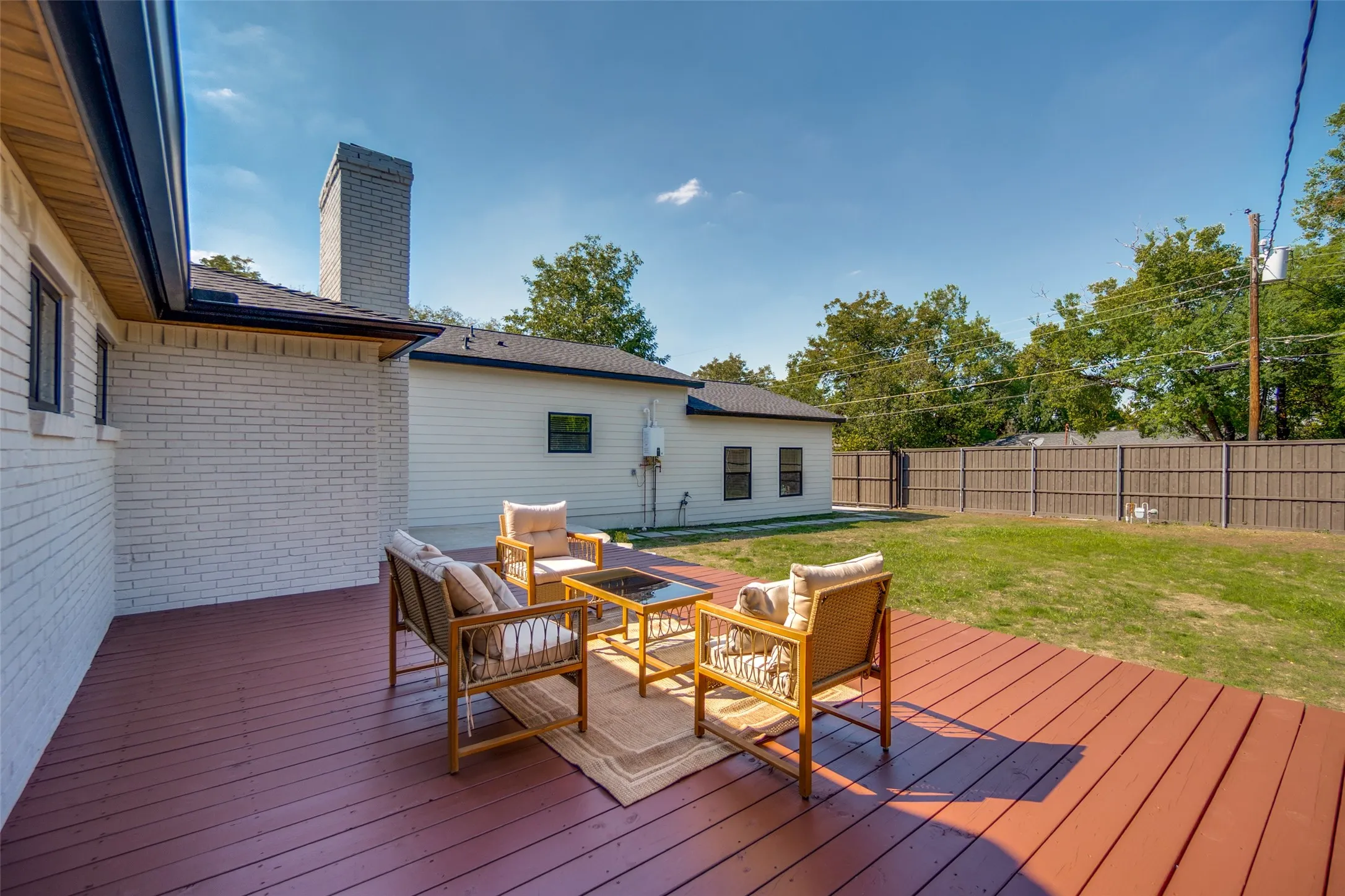 Expansive wood deck with a red-brown finish, white brick exterior, black gutters, and a gray stone chimney