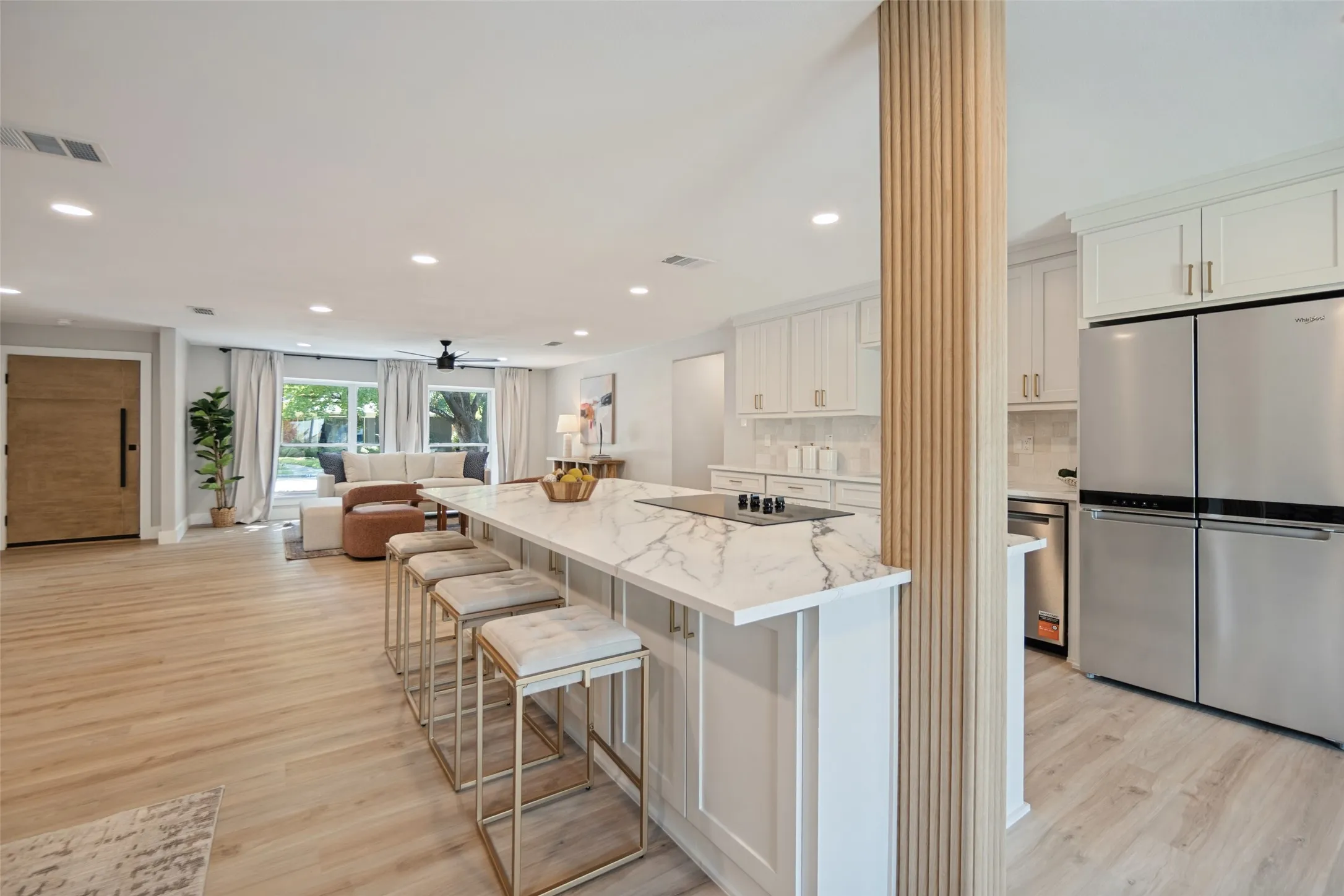 Open-concept living space featuring wood-finish flooring, a kitchen island with stone countertop, built-in cooktop, and a stainless steel refrigerator