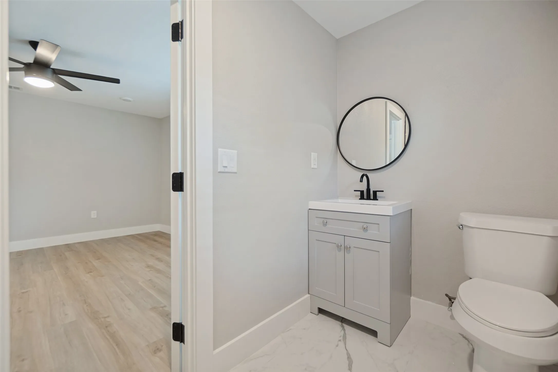 Light gray vanity with an integrated sink, matte black faucet, and a round black-framed mirror