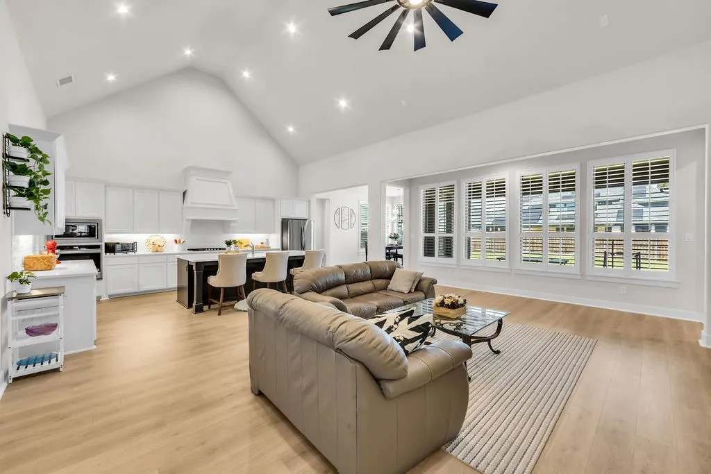 Vaulted ceiling with recessed lighting and a ceiling fan, wood-finish flooring, white kitchen cabinetry, a kitchen island, and multiple windows with plantation shutters