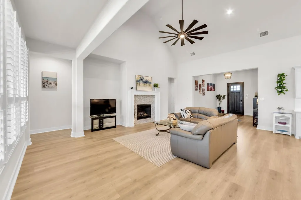 Vaulted ceiling with a contemporary ceiling fan, wood-finish flooring, and a fireplace with a decorative tile surround