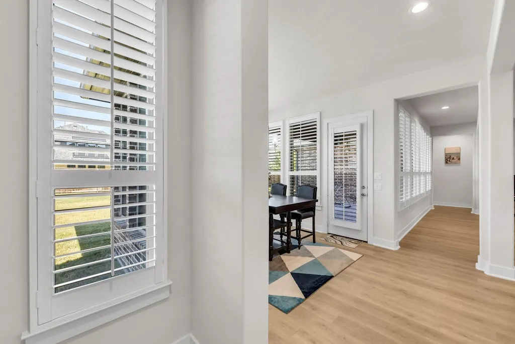 Plantation shutters, light wood-finish flooring, recessed lighting, white trim, and a white interior door
