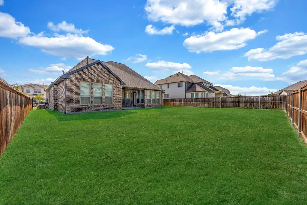 Expansive backyard featuring a manicured lawn, full wood fencing, and a brick exterior home with a covered patio