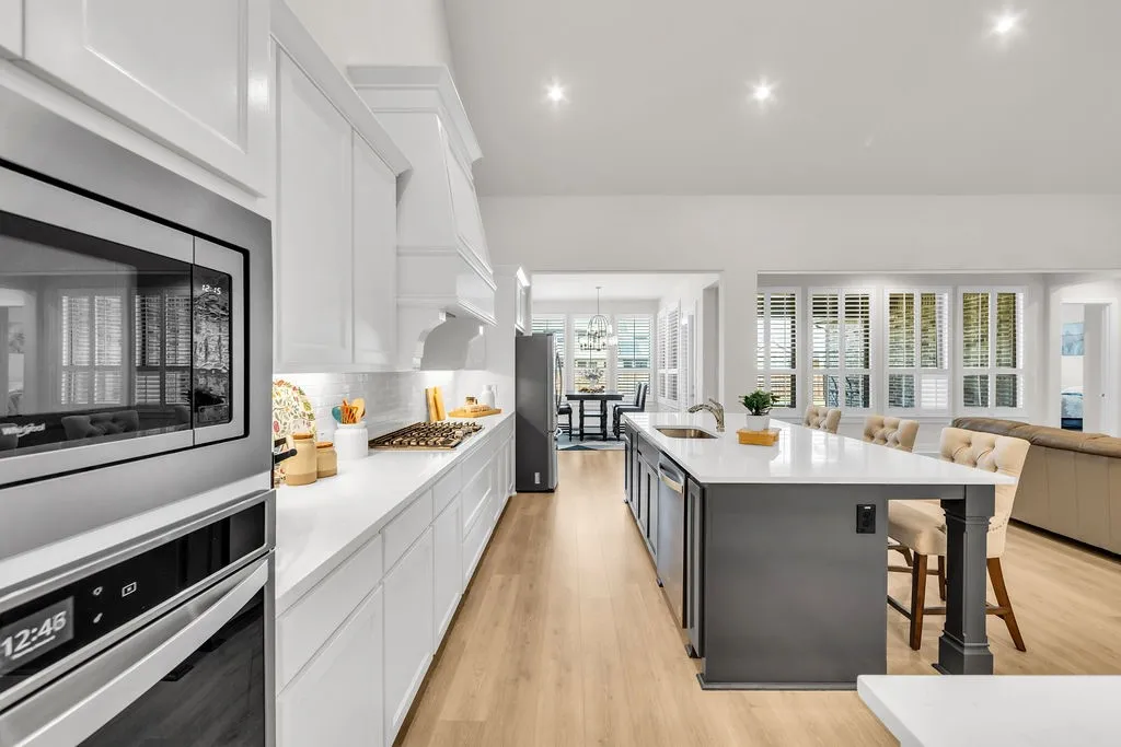 Gourmet kitchen with built-in stainless steel appliances, white cabinetry, a large center island with seating, and light wood-finish flooring