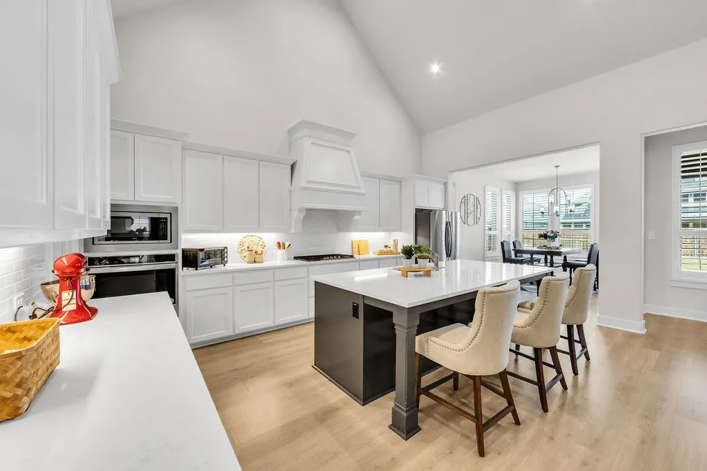 Gourmet kitchen with vaulted ceiling, white cabinetry, integrated stainless steel appliances, a large center island with counter seating, and wood-finish flooring