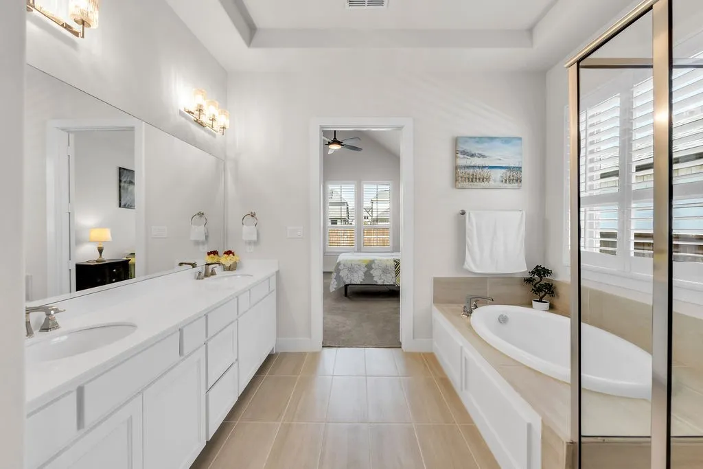 Dual vanity with undermount sinks, built-in soaking tub, framed glass shower enclosure, and light-toned tile flooring