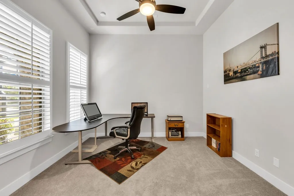 Tray ceiling with a ceiling fan, two windows with plantation shutters, light gray wall paint, and light gray carpeting