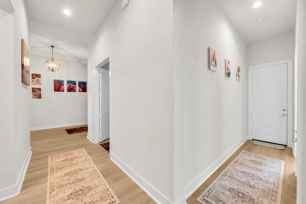 Hallway featuring wood-finish flooring, recessed lighting, a paneled door, and a geometric chandelier