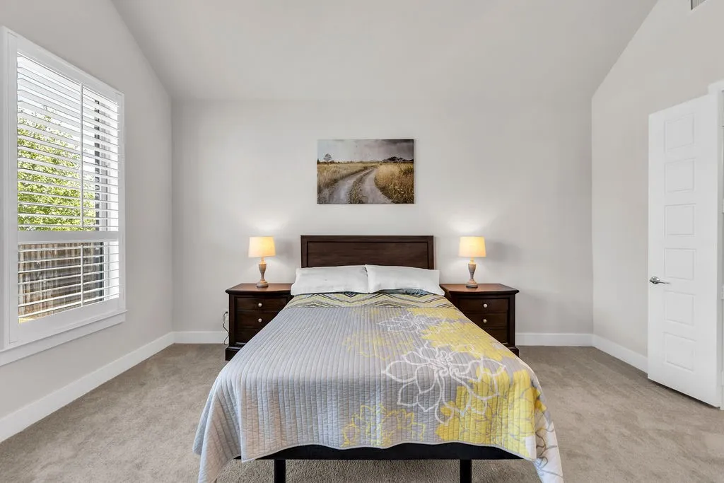 Vaulted ceiling, window with plantation shutters, light-toned carpeting, white interior door with contemporary hardware