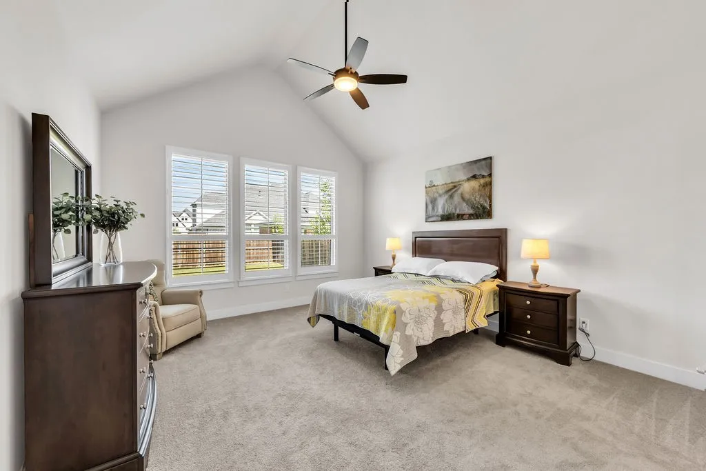 Vaulted ceiling featuring a ceiling fan, plush carpeting, and a three-pane window with plantation shutters