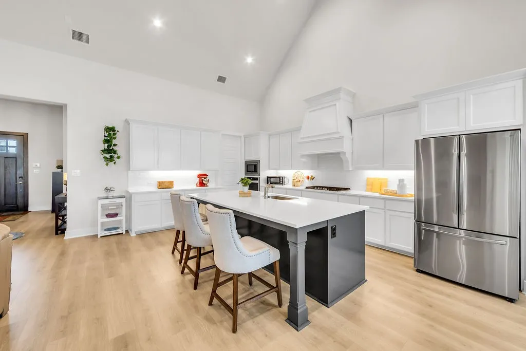 High vaulted ceiling, wood-finish flooring, white cabinetry with crown molding, stainless steel French door refrigerator, and a kitchen island with seating