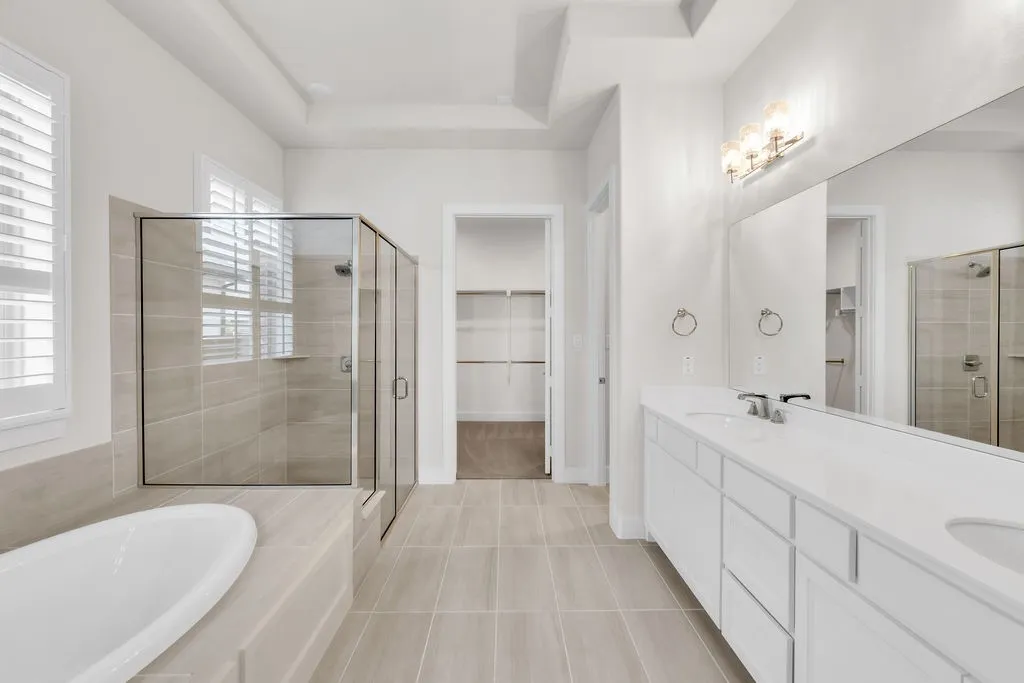 Dual vanity with integrated sinks, recessed ceiling, freestanding bathtub, walk-in shower with glass enclosure, and plantation shutters