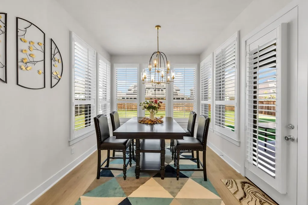 Dining area featuring wood-finish flooring, multiple windows with white plantation shutters, a glass-paned door with white plantation shutters, and a linear chandelier