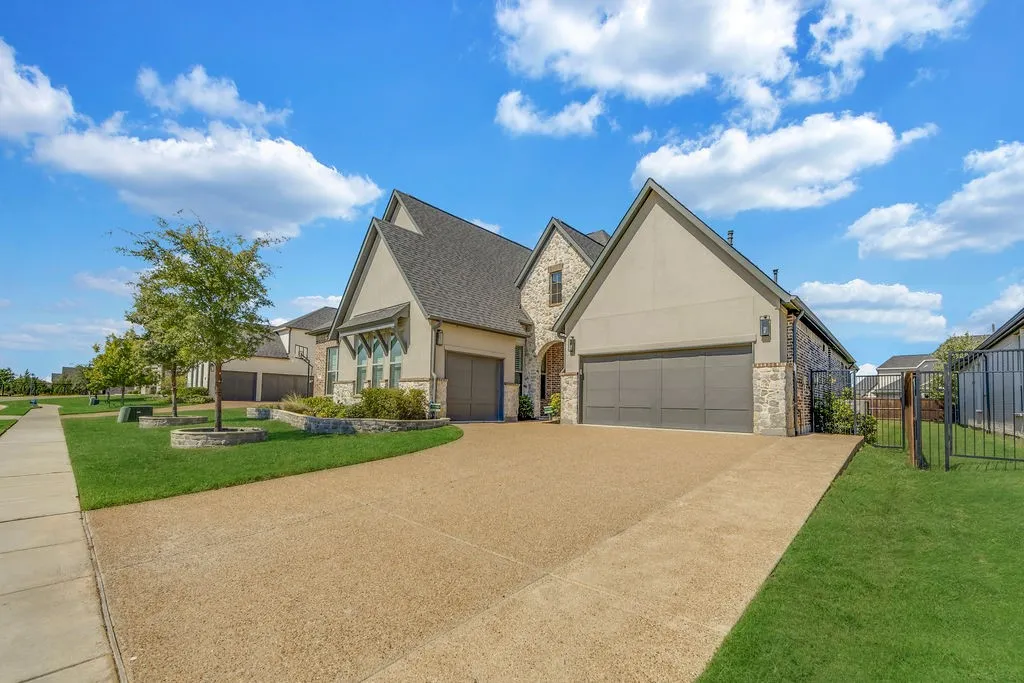 Stucco and stone exterior, gabled roofline, two integrated garages, concrete driveway, and a wrought iron fence
