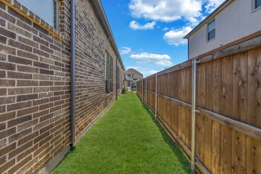 Manicured lawn area featuring a brick exterior, functional gutters, and a wood privacy fence