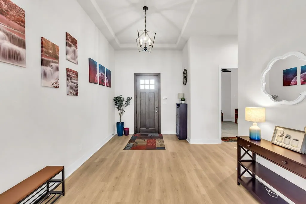 Wood-finish flooring, recessed tray ceiling, contemporary chandelier, paneled entry door, and bright white walls