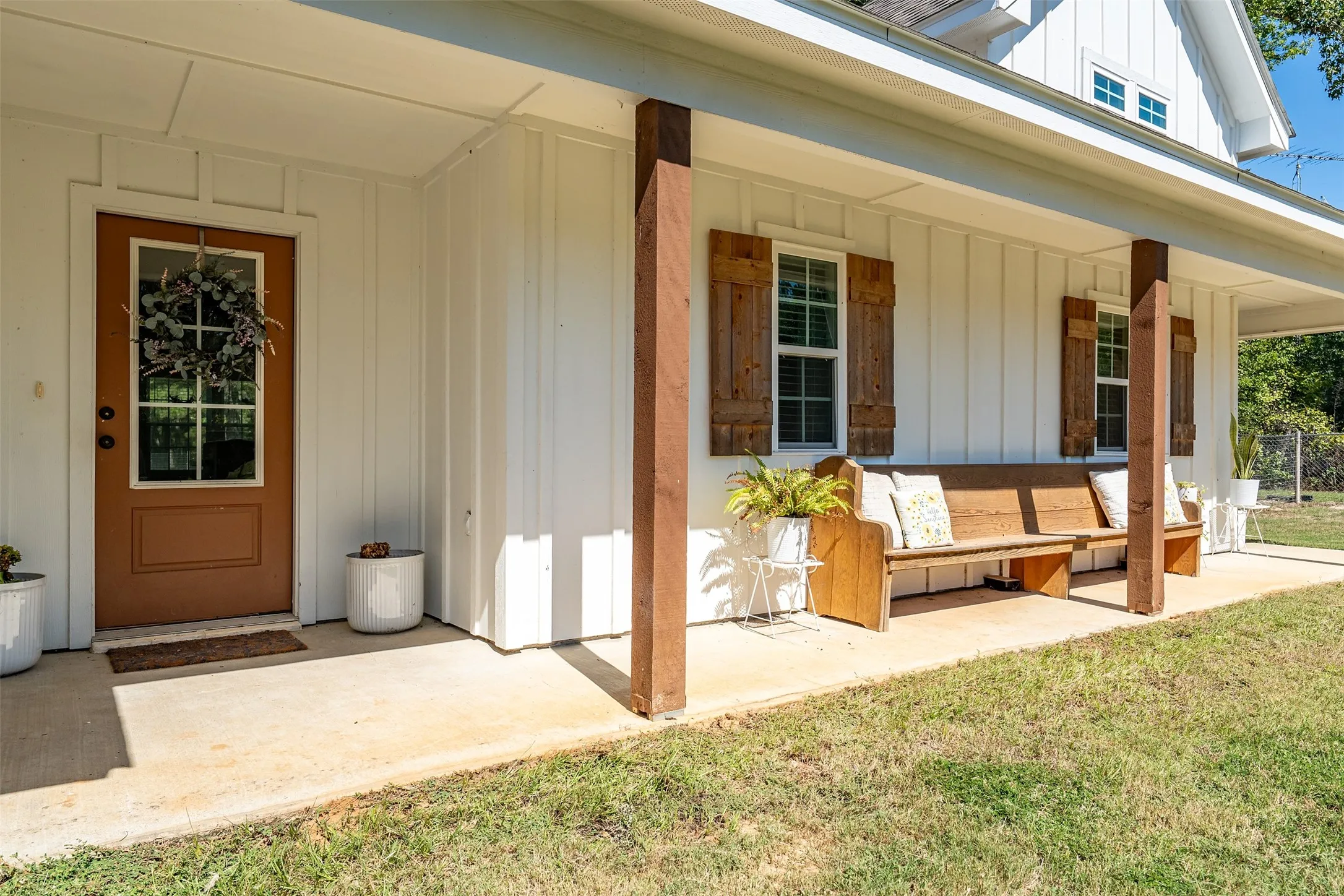 Covered porch with concrete flooring, wood structural columns, and white board-and-batten siding