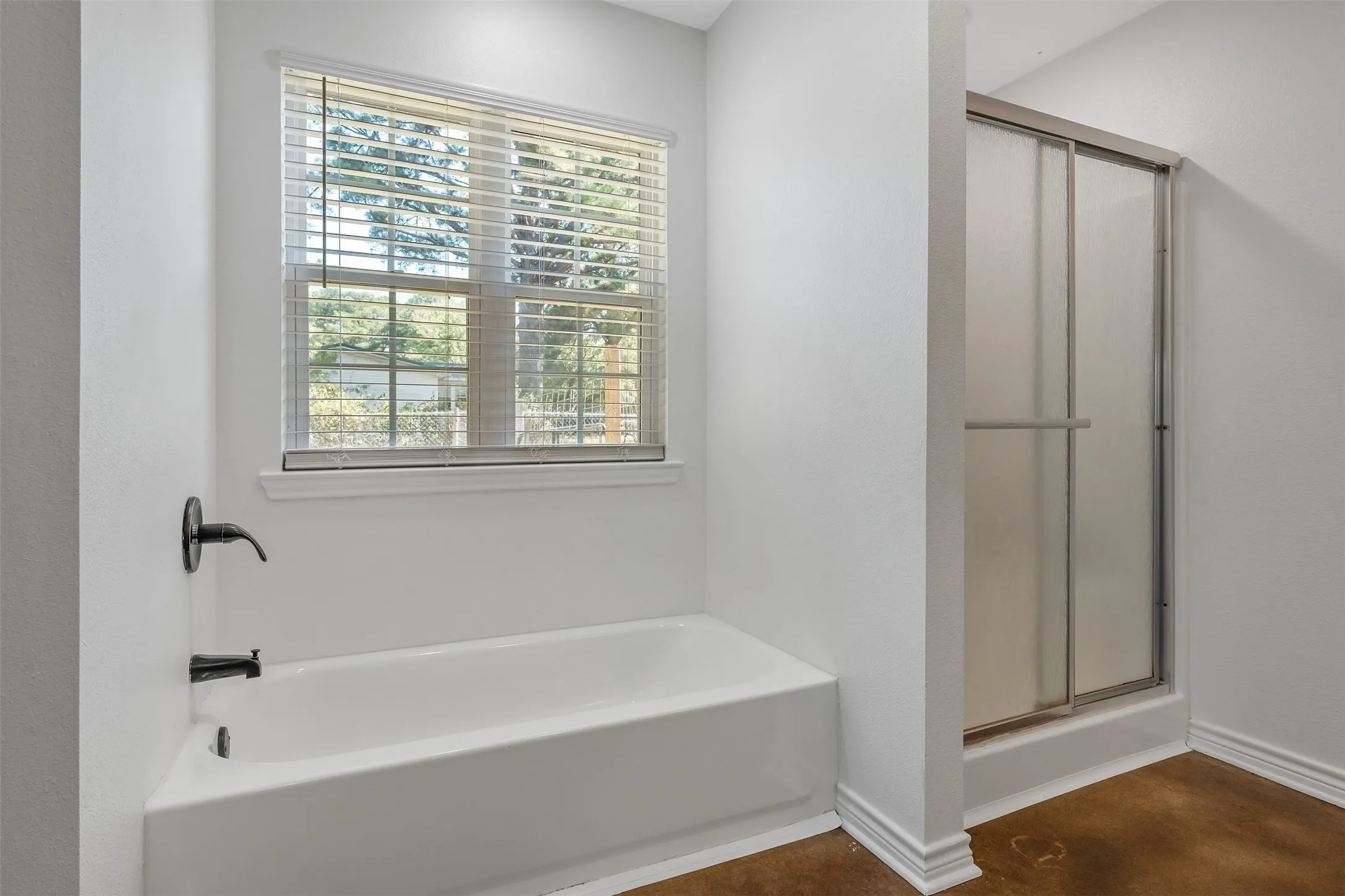 White tub with matte black fixtures, a window with blinds, and a shower with frosted sliding glass doors