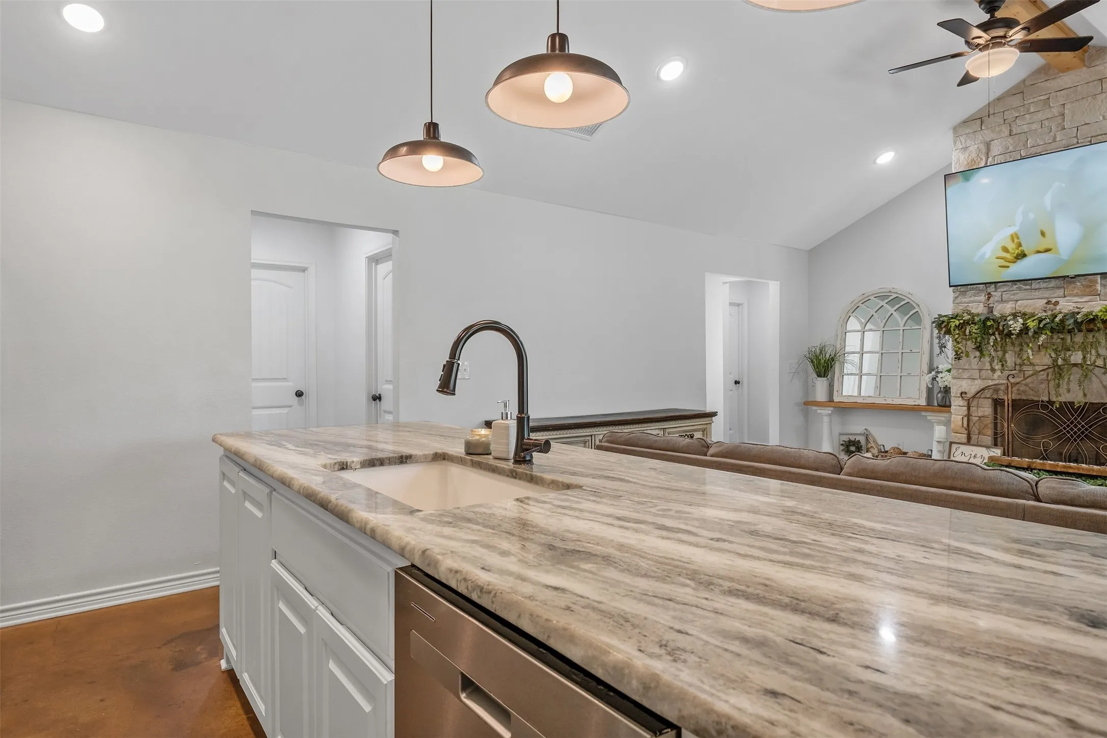 Spacious kitchen island with integrated sink, stainless steel appliance, recessed lighting, and pendant fixtures