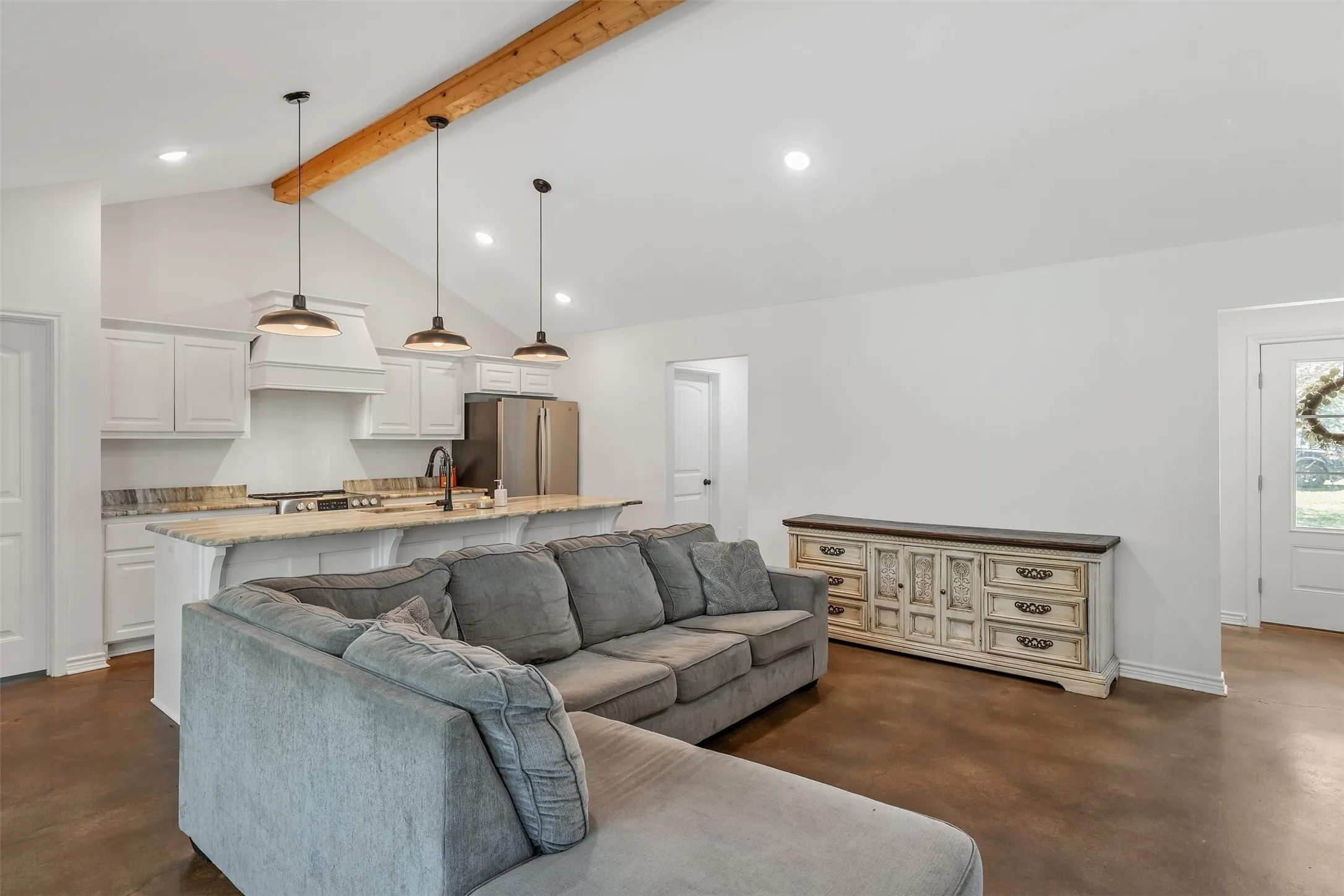 Vaulted ceiling with exposed wood beam, kitchen with white cabinetry, stainless steel appliances, and island with pendant lighting, recessed lighting, and wood-finish flooring