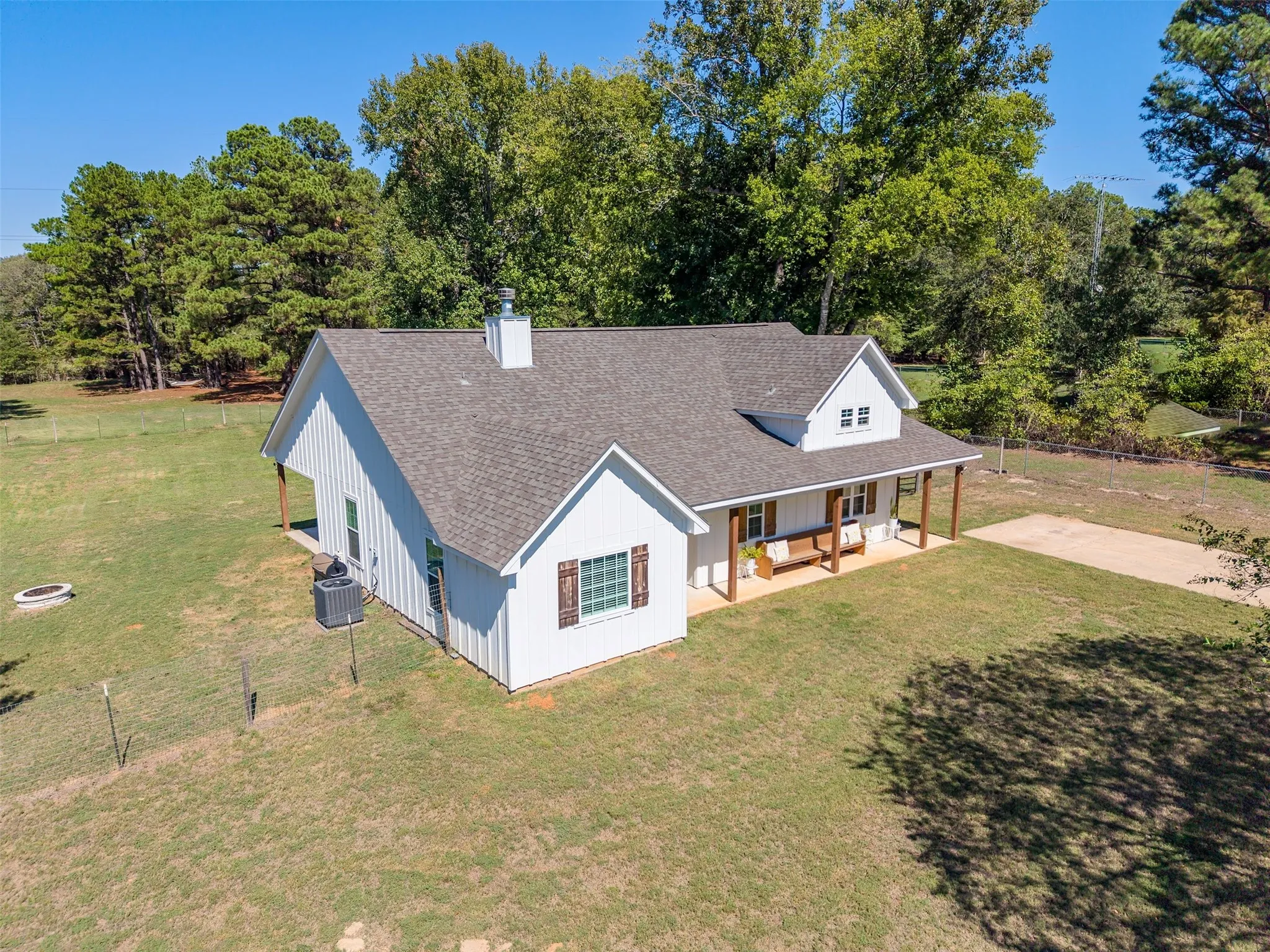 White board and batten siding, dark shingle roof, covered front porch with wood columns, dormer window, and a gravel driveway