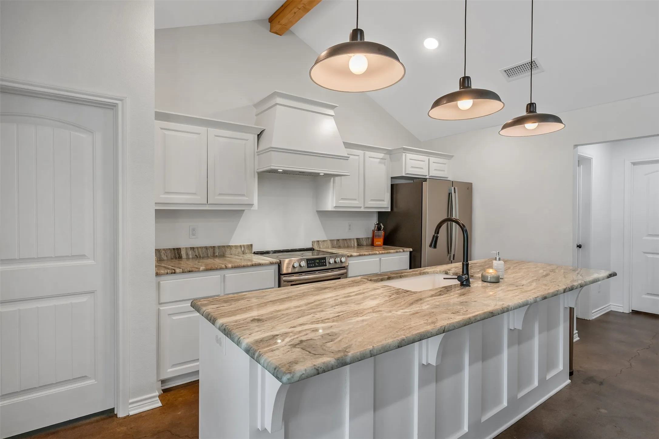 Kitchen featuring a large island with an integrated sink, stone countertops, white cabinetry, and stainless steel appliances