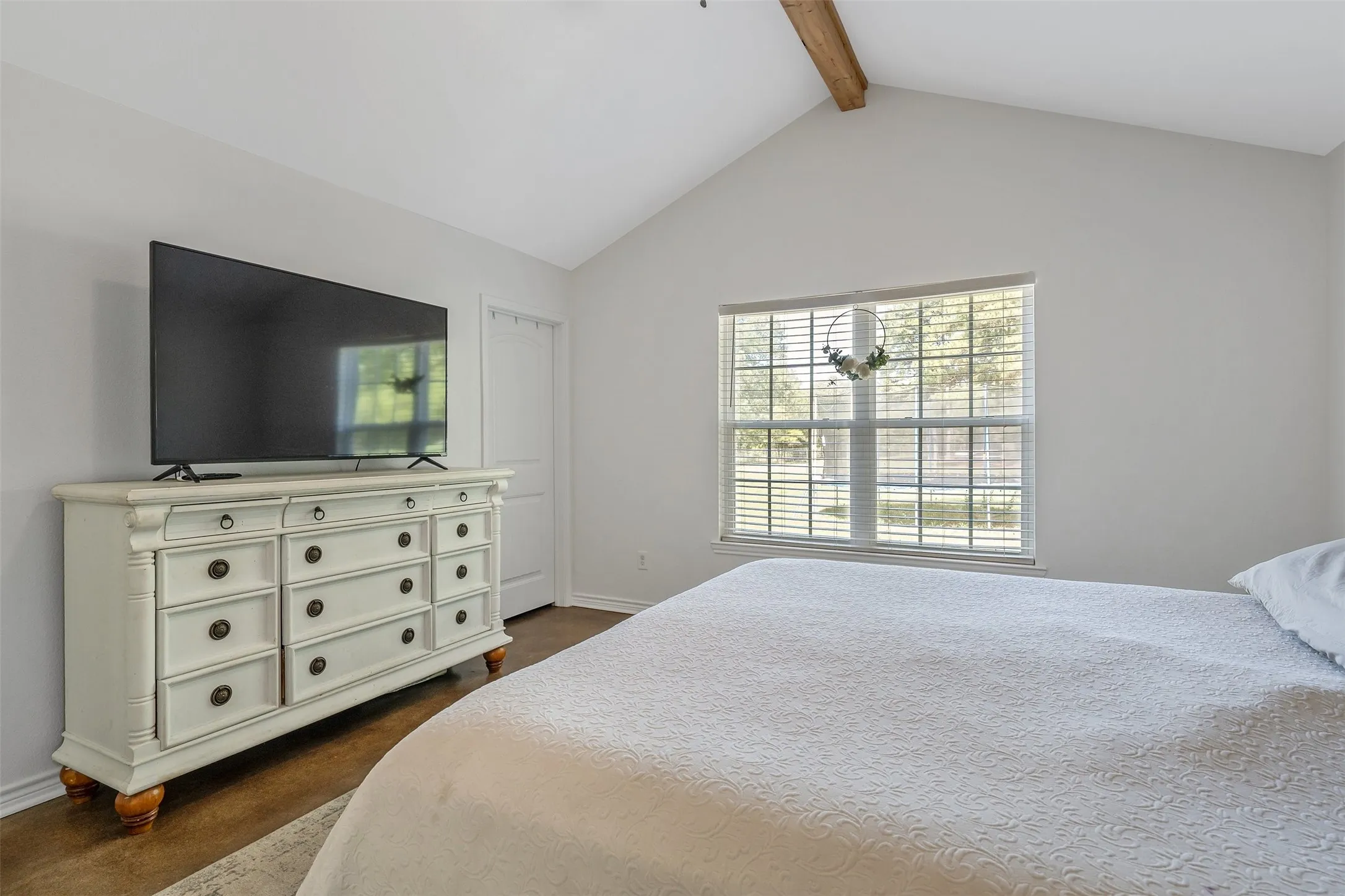 Vaulted ceiling with an exposed wood beam, large window with blinds, and durable flooring