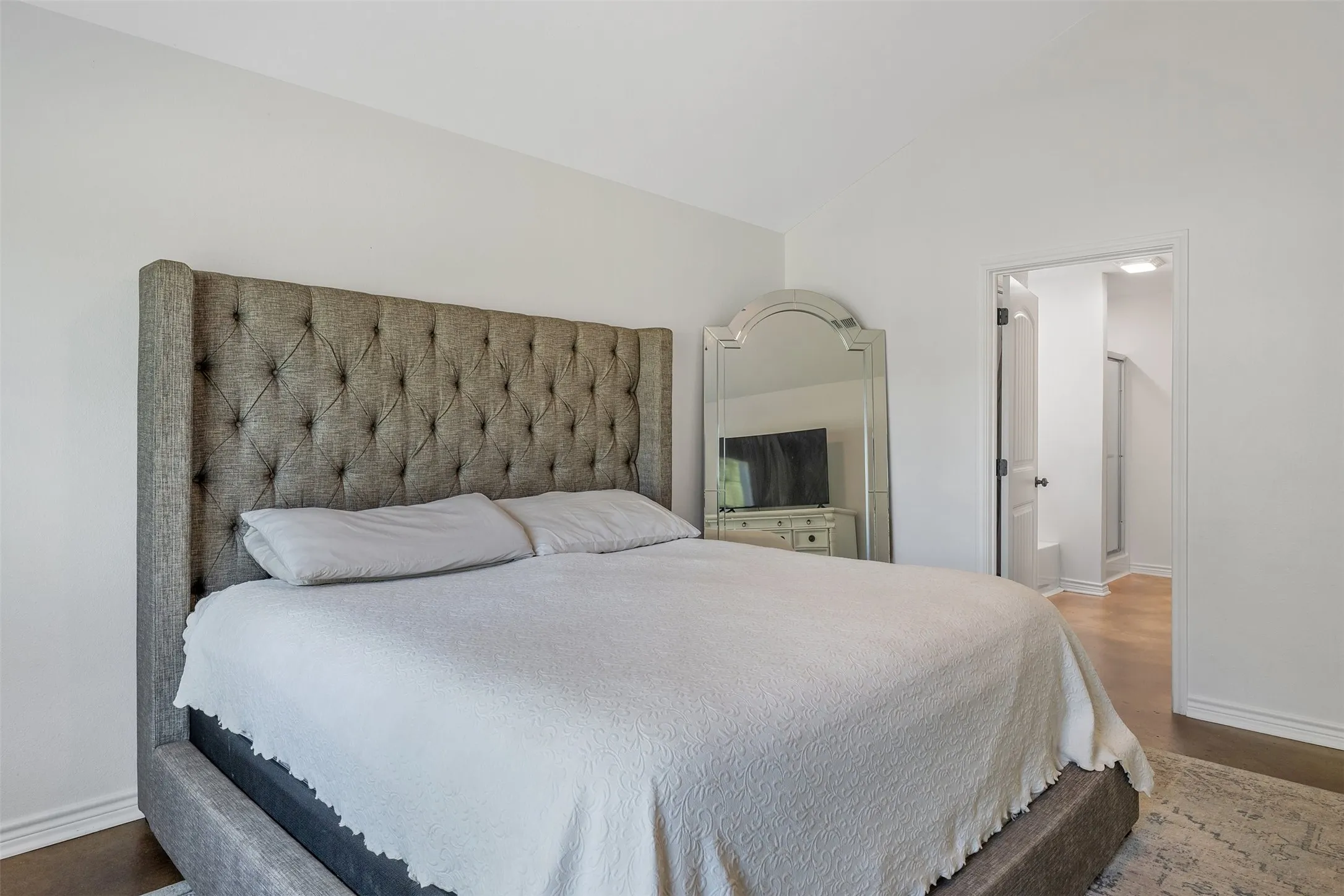 Vaulted ceiling with a neutral color palette, wood-finish flooring, and recessed doorway leading to an additional space