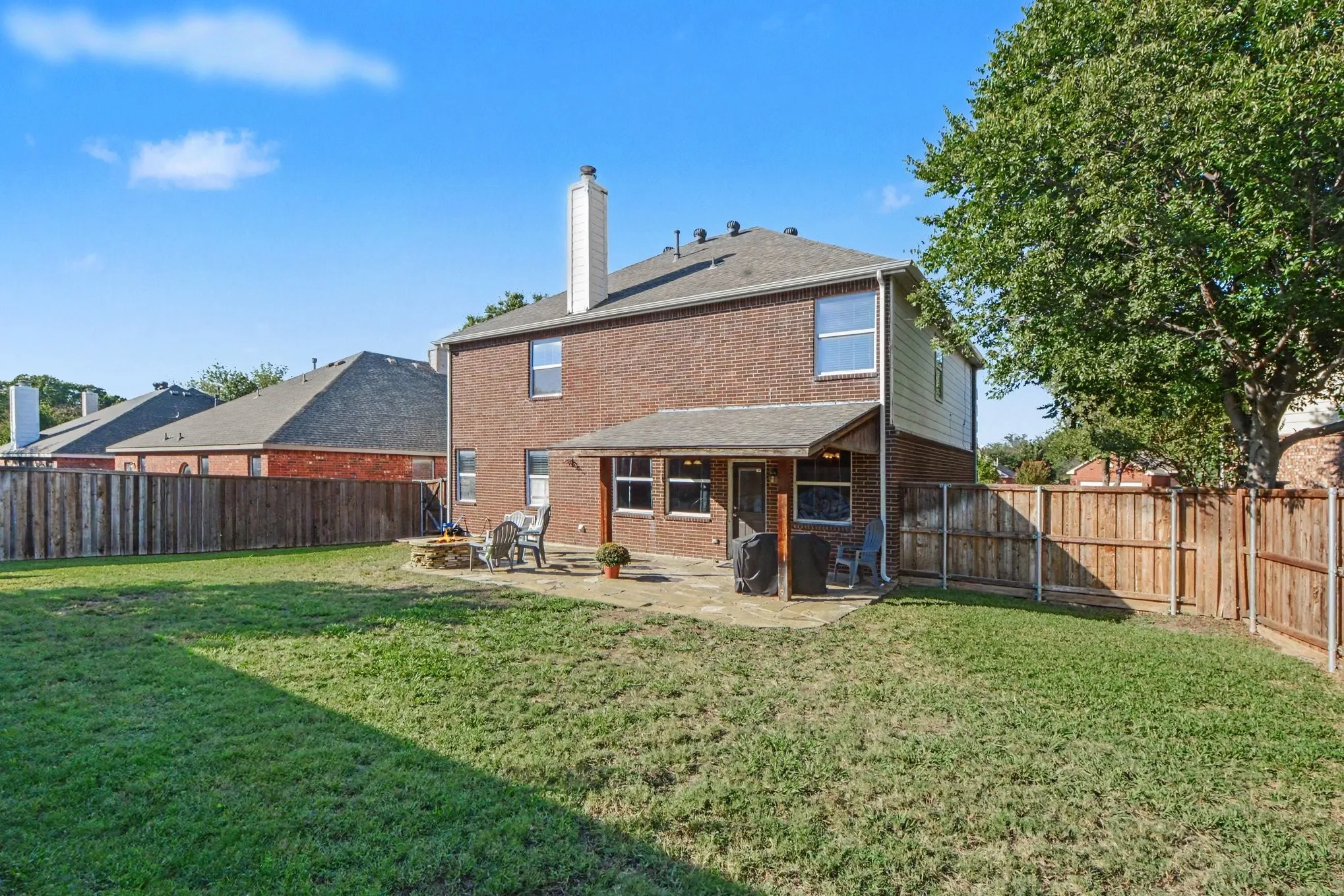 Expansive backyard featuring a brick exterior, covered patio, stone patio, and wood privacy fencing