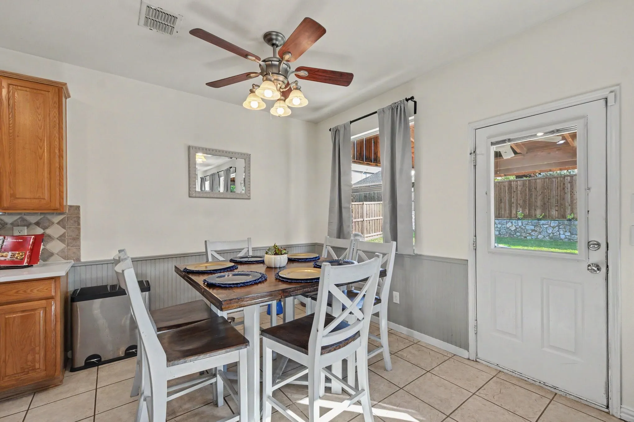 Tiled flooring, warm wood-finish cabinetry, patterned backsplash, ceiling fan with integrated lighting, and a glass-paneled exterior door