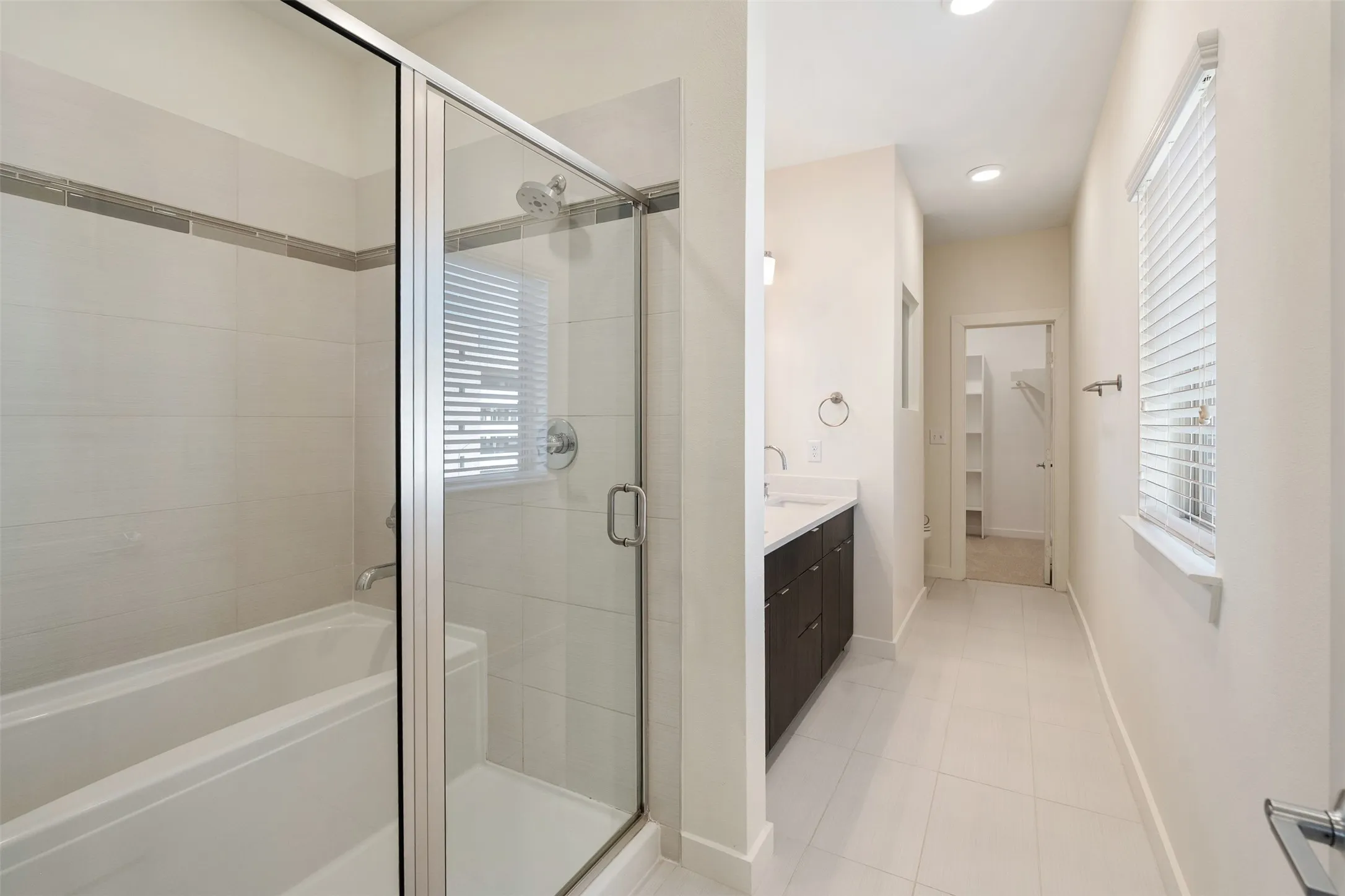 Bathroom featuring a glass-enclosed shower, bathtub, dual-sink vanity with dark cabinetry, tile flooring, and recessed lighting