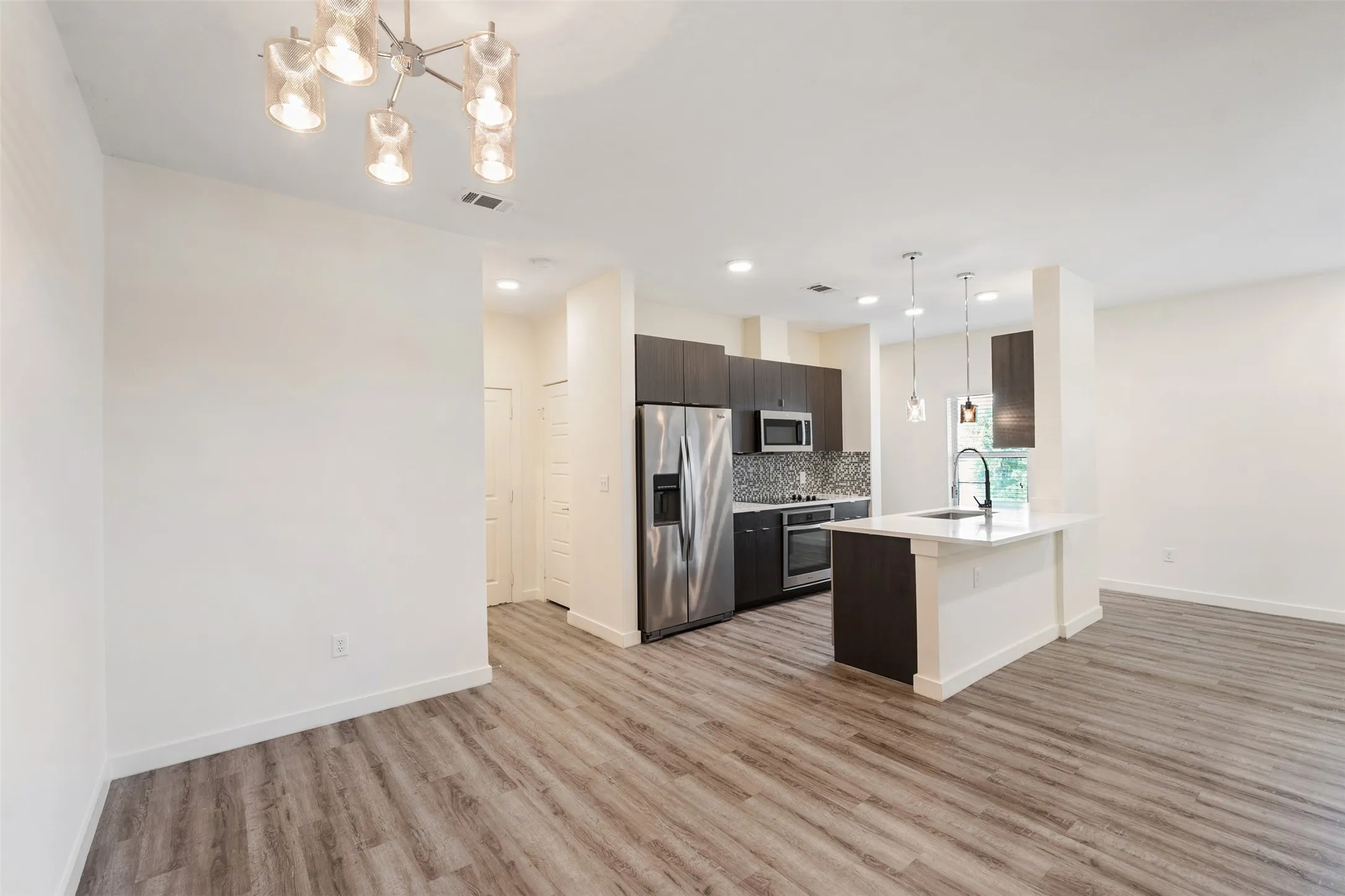 Open-concept living space with wood-finish flooring, modern kitchen, stainless steel appliances, and an island with pendant lighting