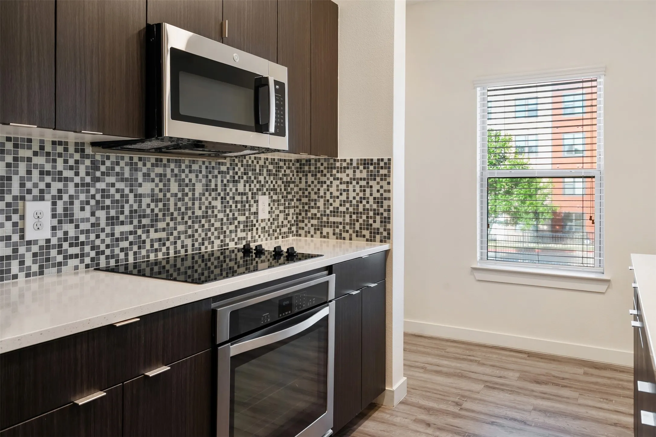 Kitchen featuring dark wood-finish cabinetry, stainless steel appliances, mosaic tile backsplash, light-toned countertops, and wood-finish flooring
