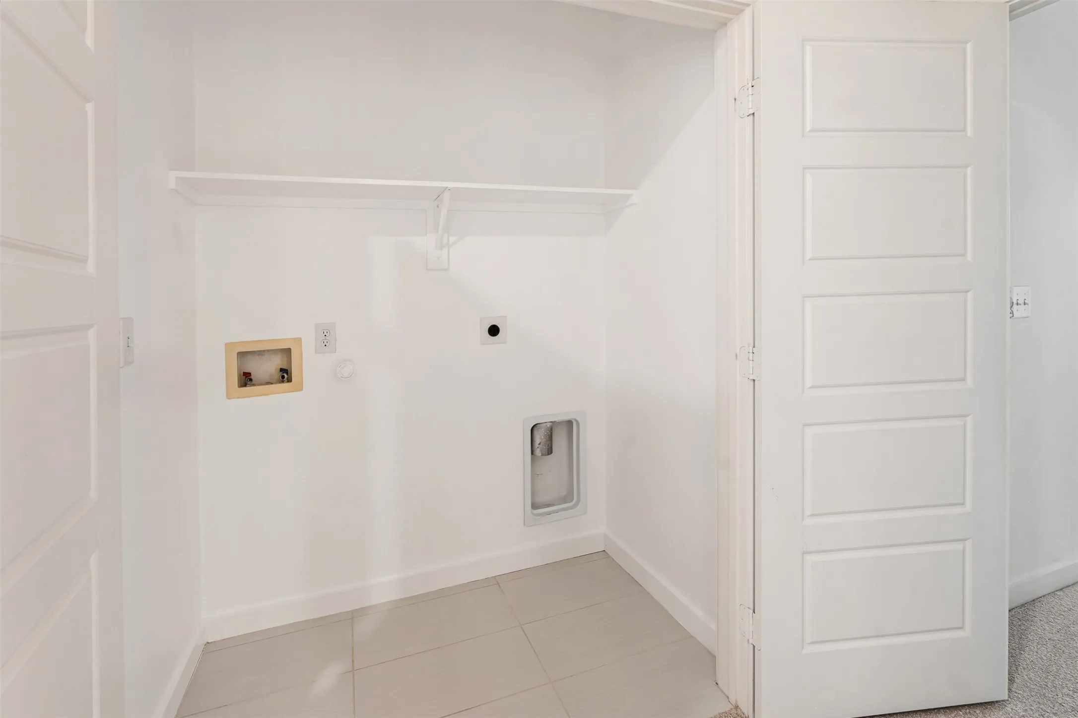 Laundry area featuring tile flooring, a white shelving unit, and a panel door