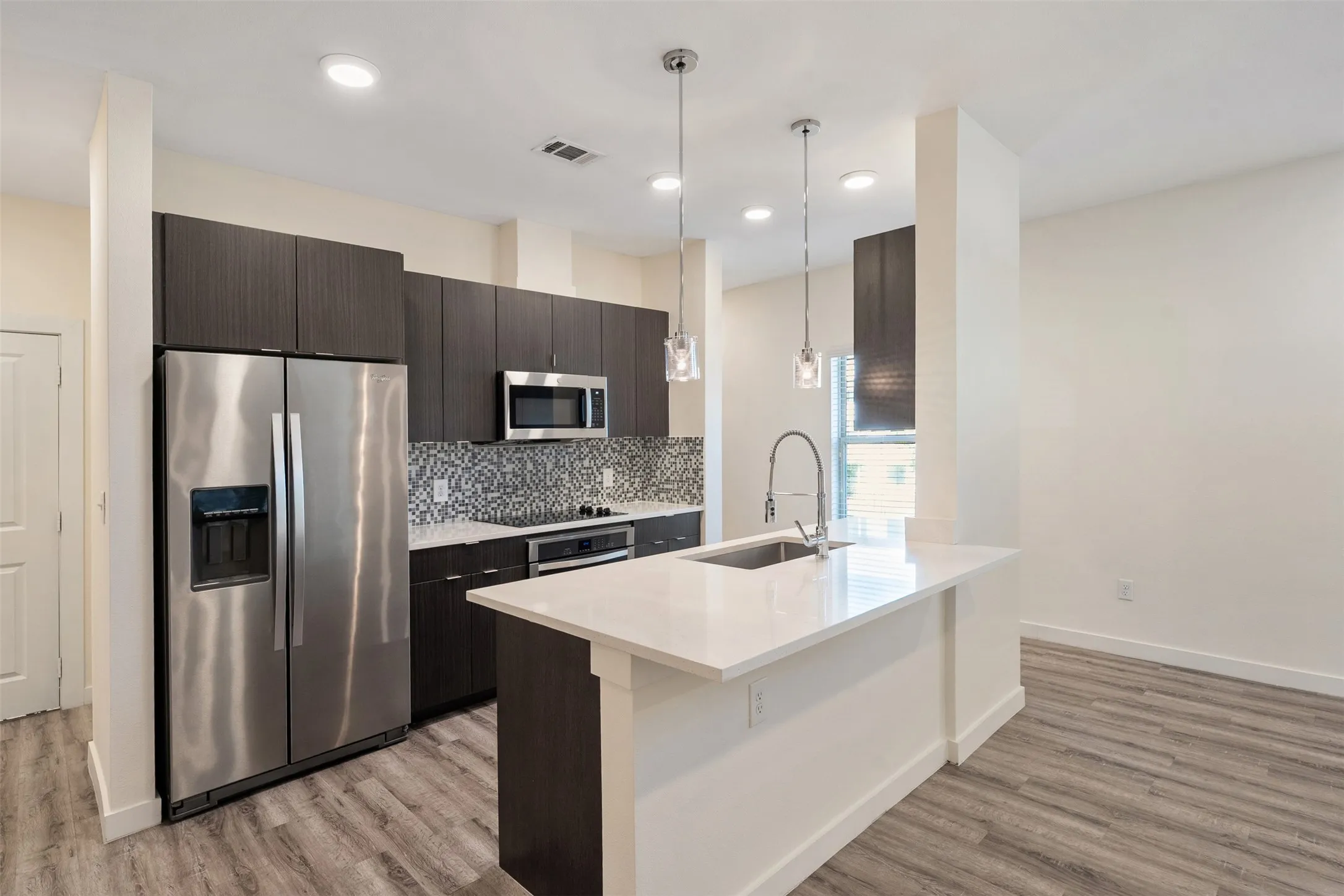 Kitchen featuring stainless steel appliances, dark wood-finish cabinetry, a patterned tile backsplash, white countertops, and wood-finish flooring