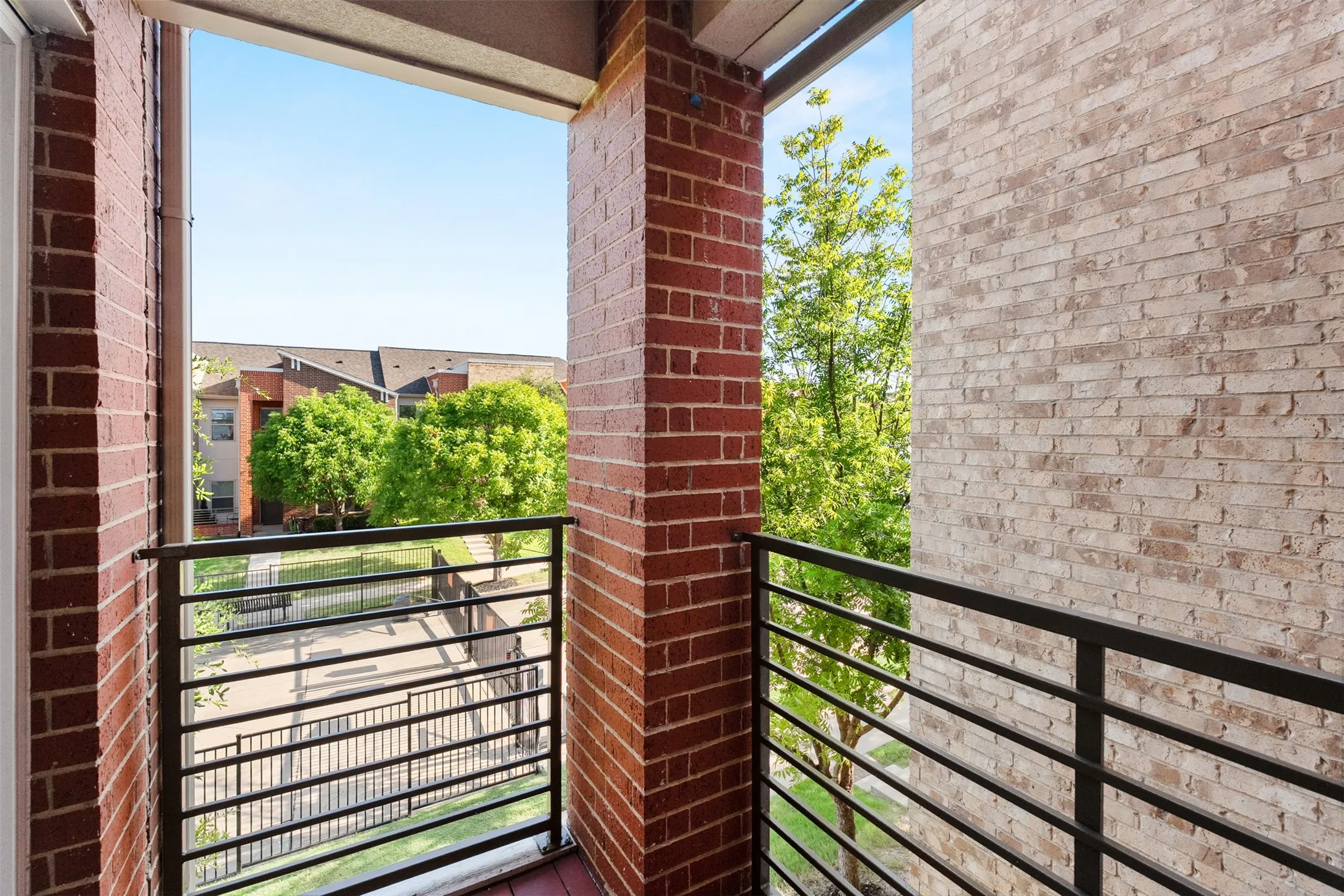 Balcony with brick columns, black metal railing, and wood-finish flooring