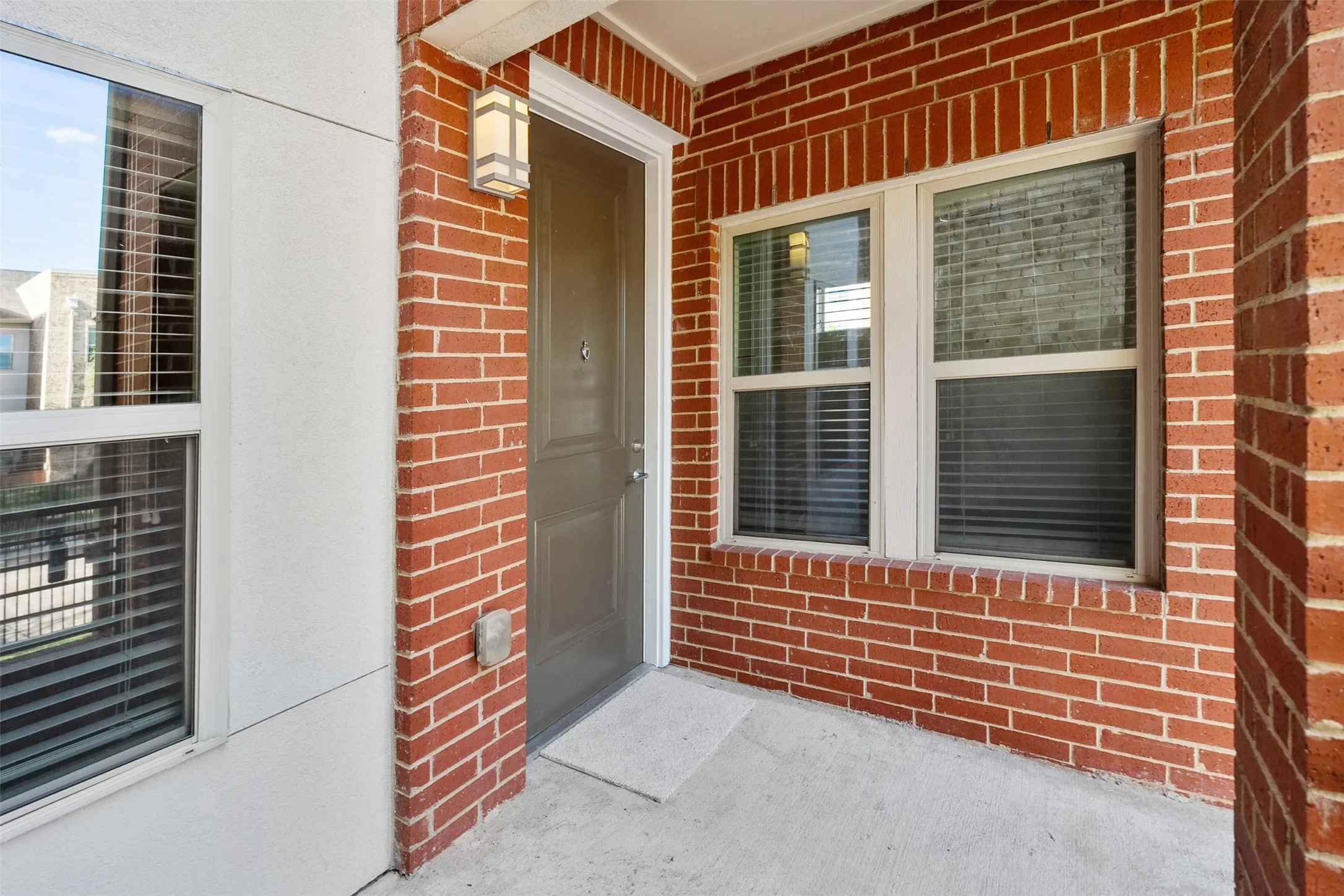 Brick exterior detailing, recessed entry, sconce lighting, and multiple windows with blinds