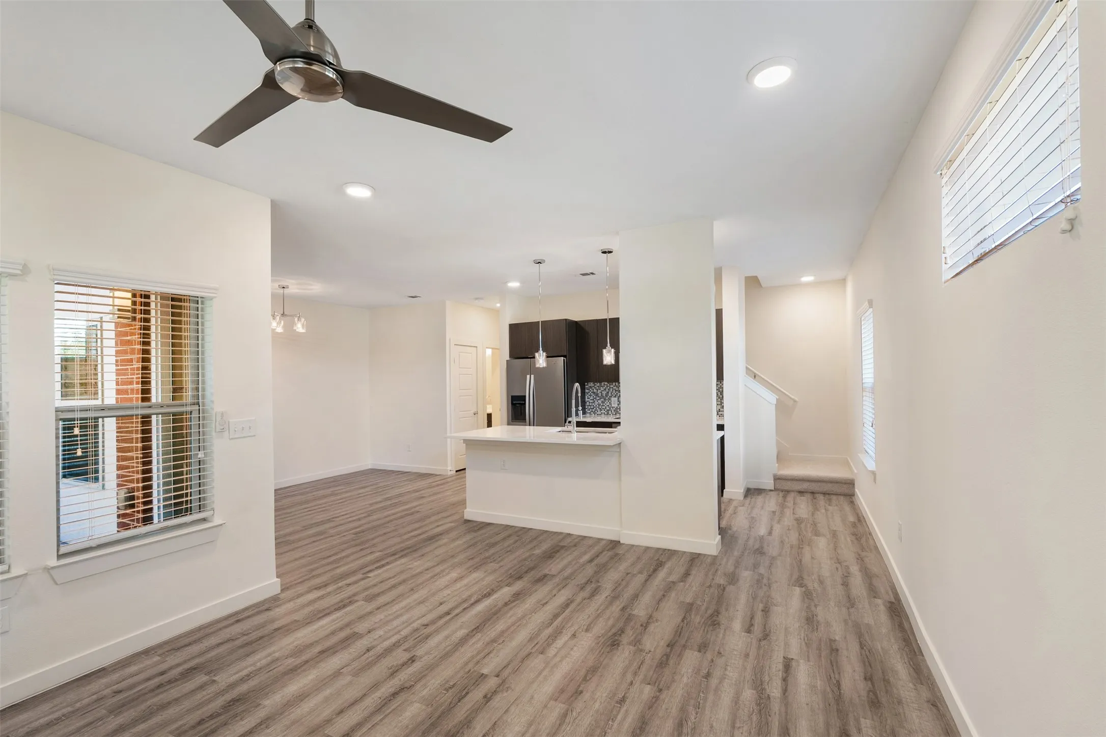Spacious open-concept living area featuring wood-finish flooring, recessed lighting, a modern ceiling fan, and a kitchen island with pendant lighting