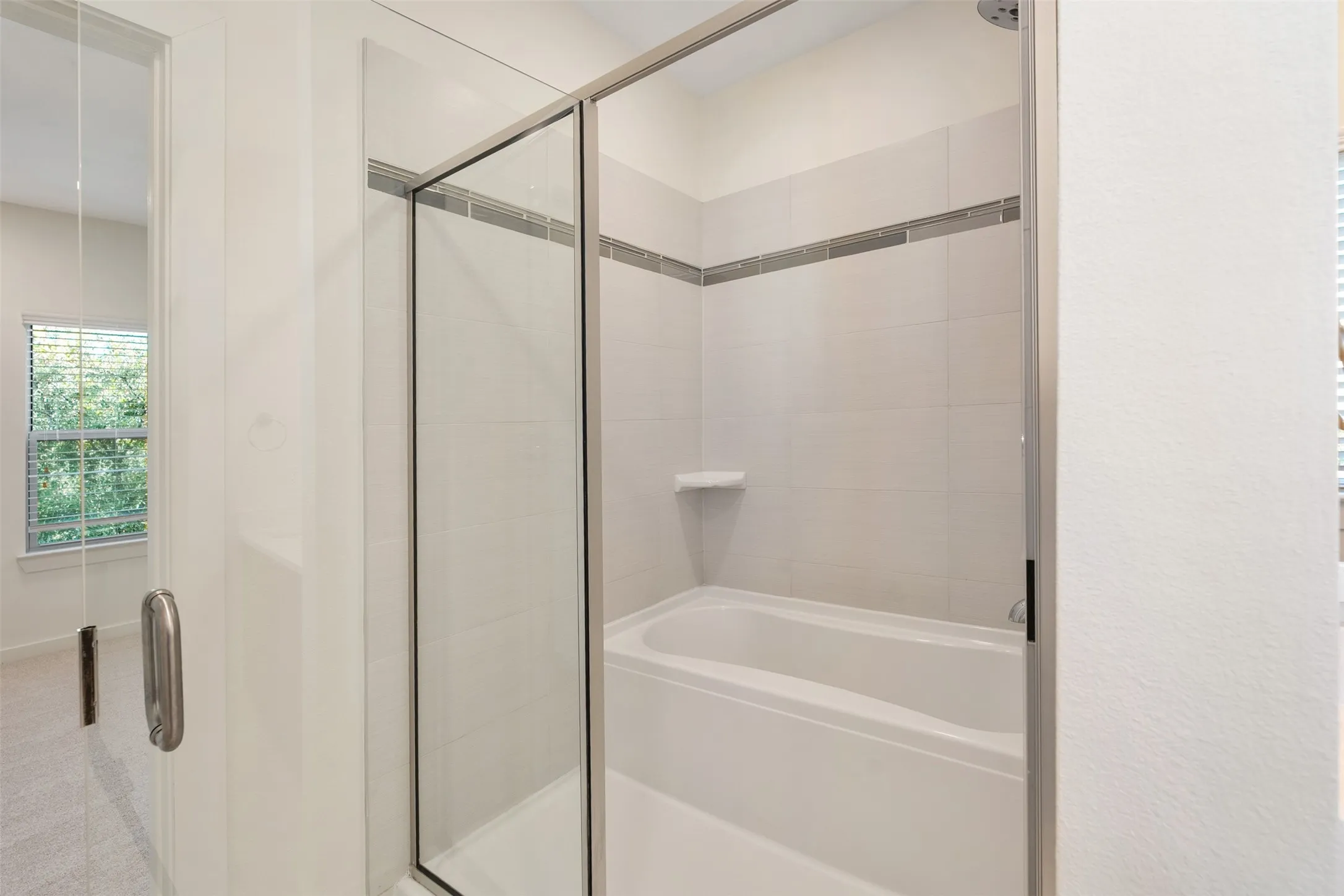 Glass-enclosed shower with a built-in tub, white tile surround, and a decorative accent tile band
