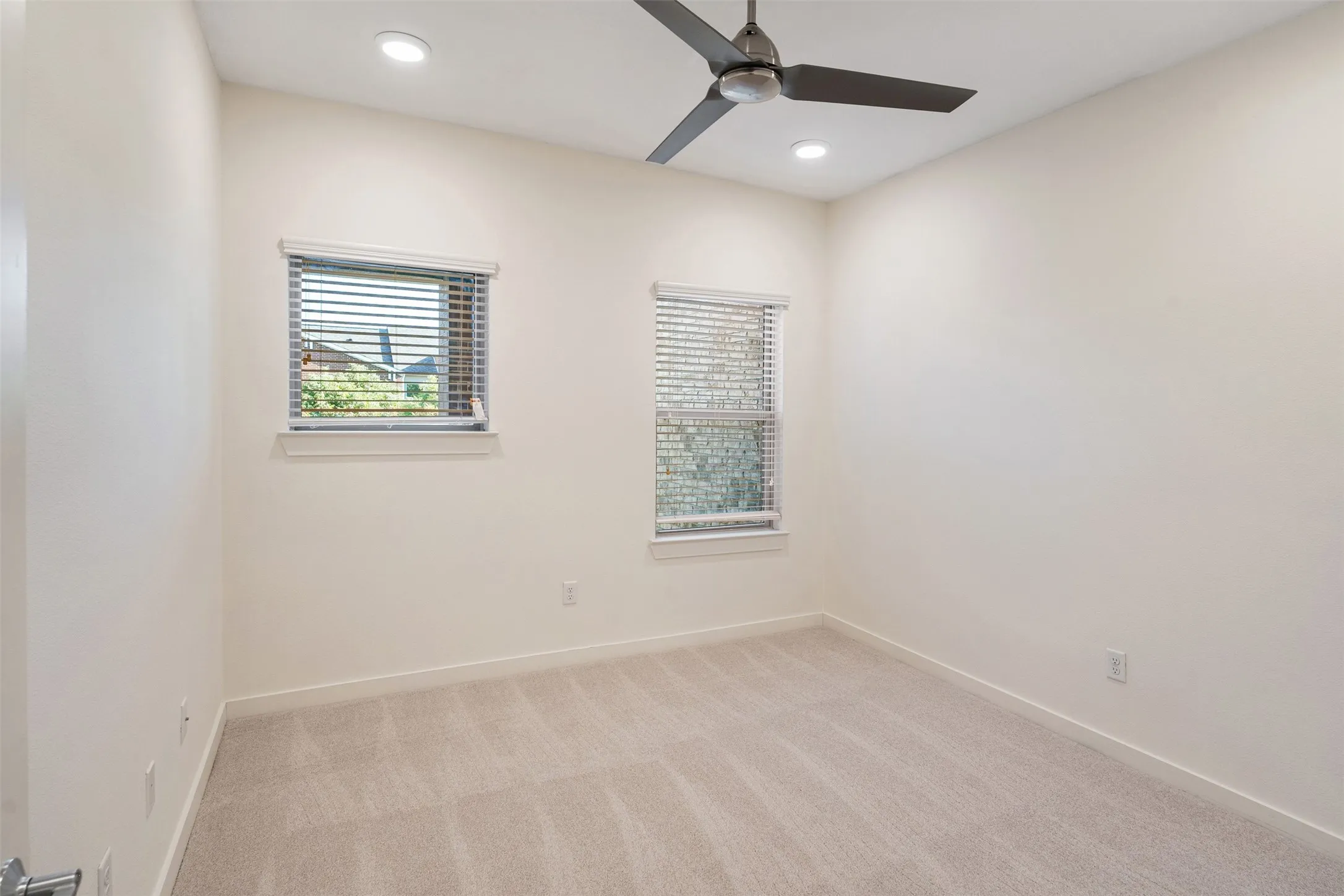 Recessed ceiling lighting, ceiling fan, two windows with blinds, and light-toned carpeting