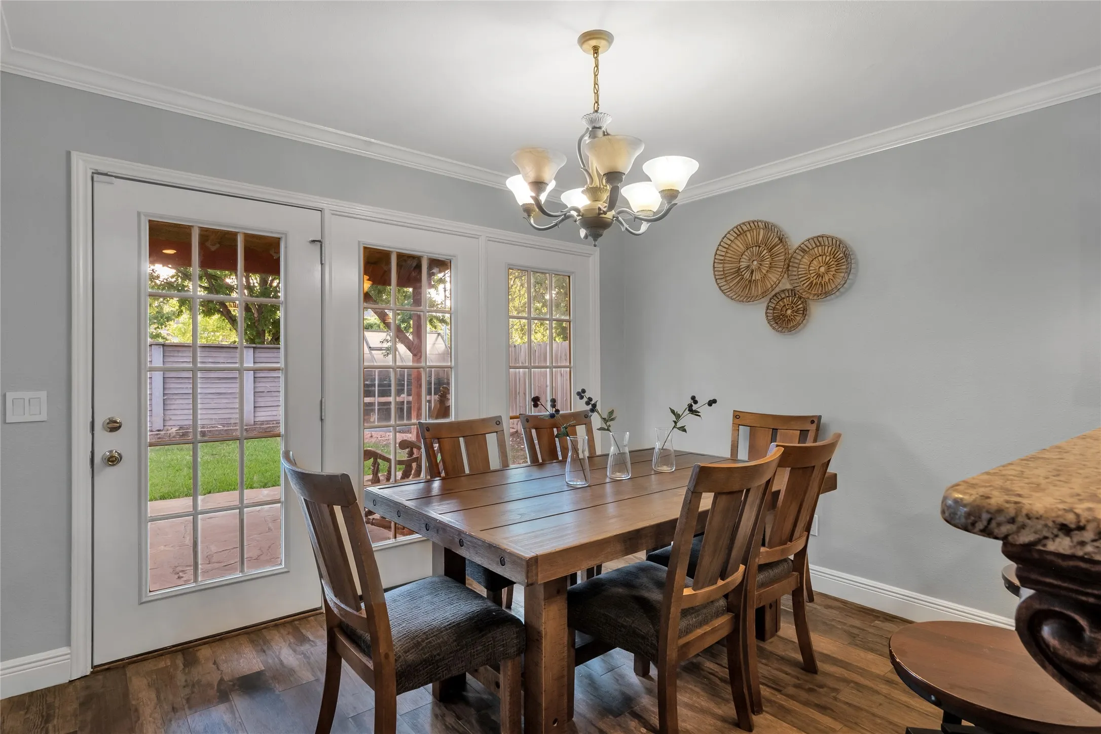 Wood-finish flooring, crown molding, and a multi-light chandelier illuminate this dining area