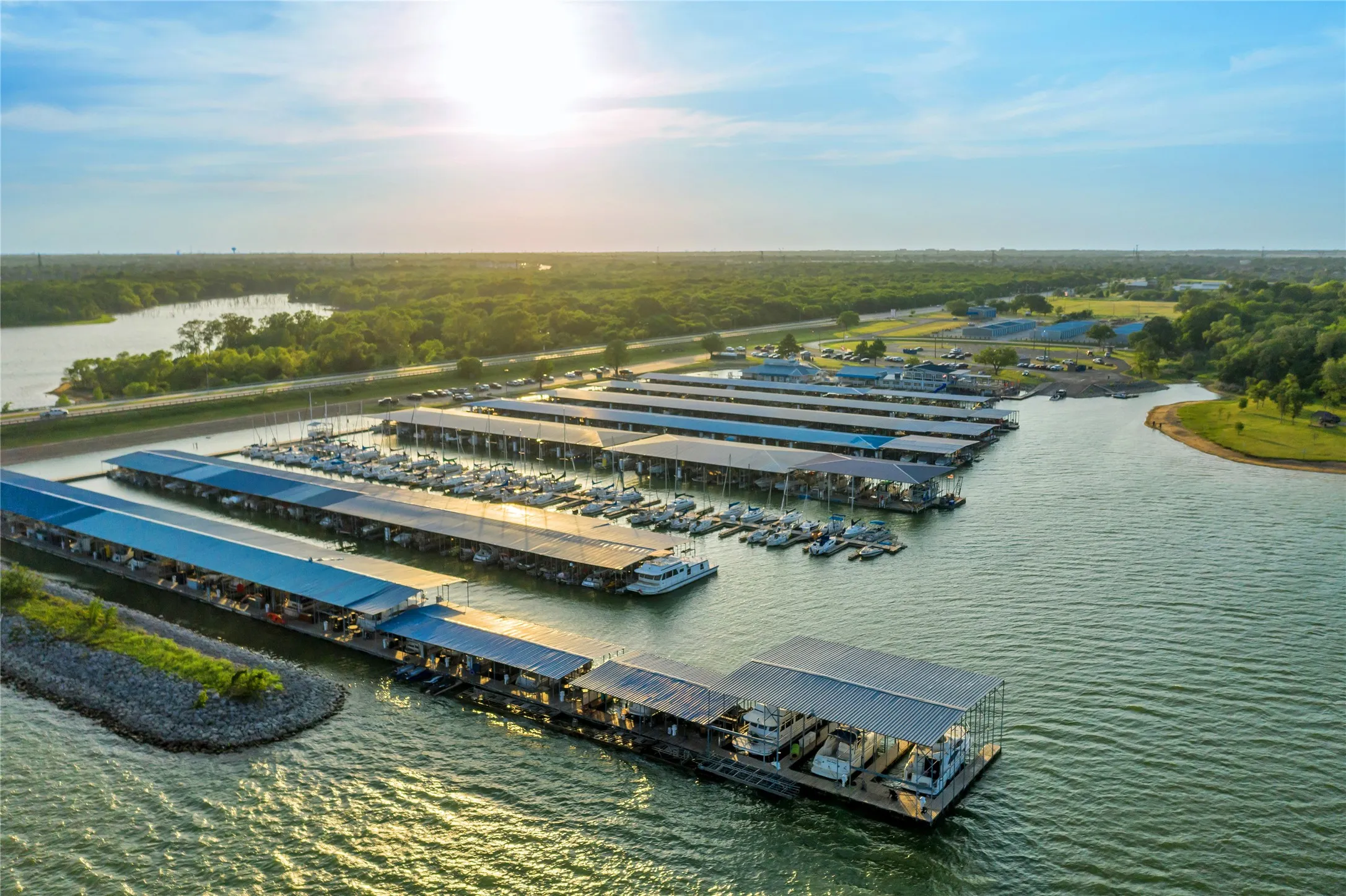 Marina with covered boat slips, surrounded by a body of water and lush green landscape