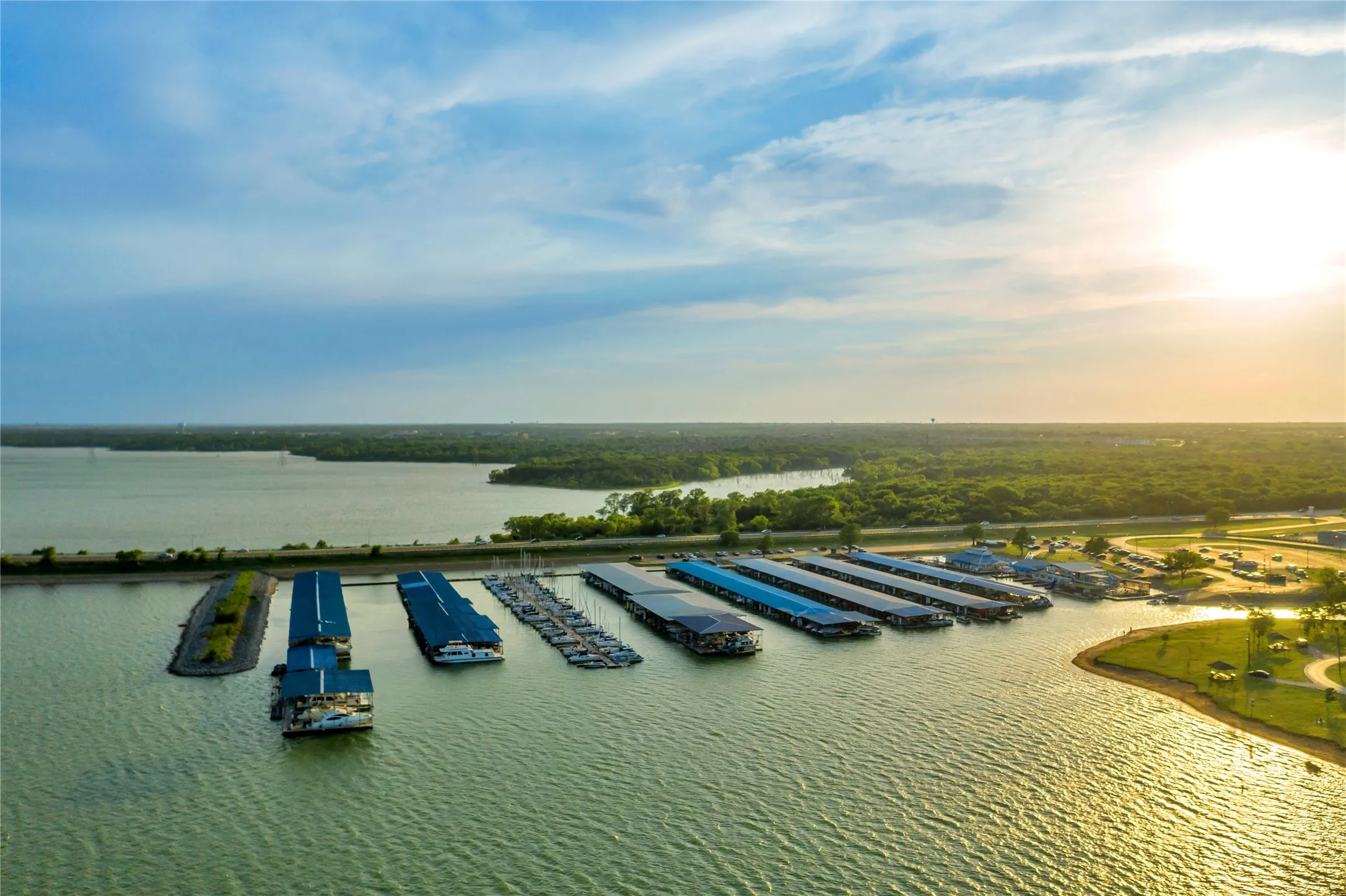 Marina with numerous covered boat slips, expansive open water, and surrounding green spaces