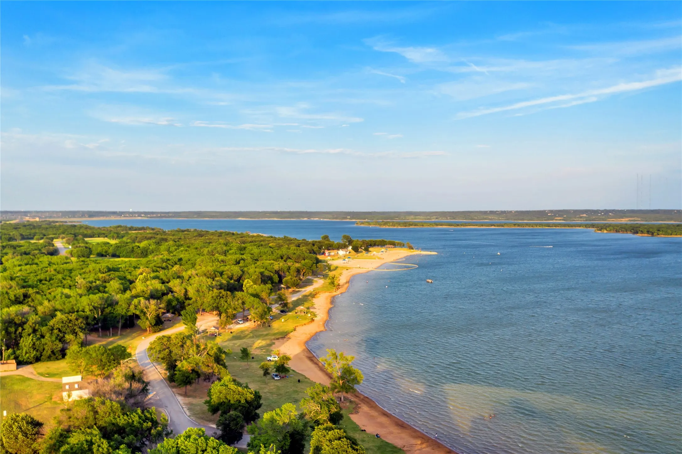 Expansive waterfront setting with a sandy shoreline, mature trees, and a clear blue sky